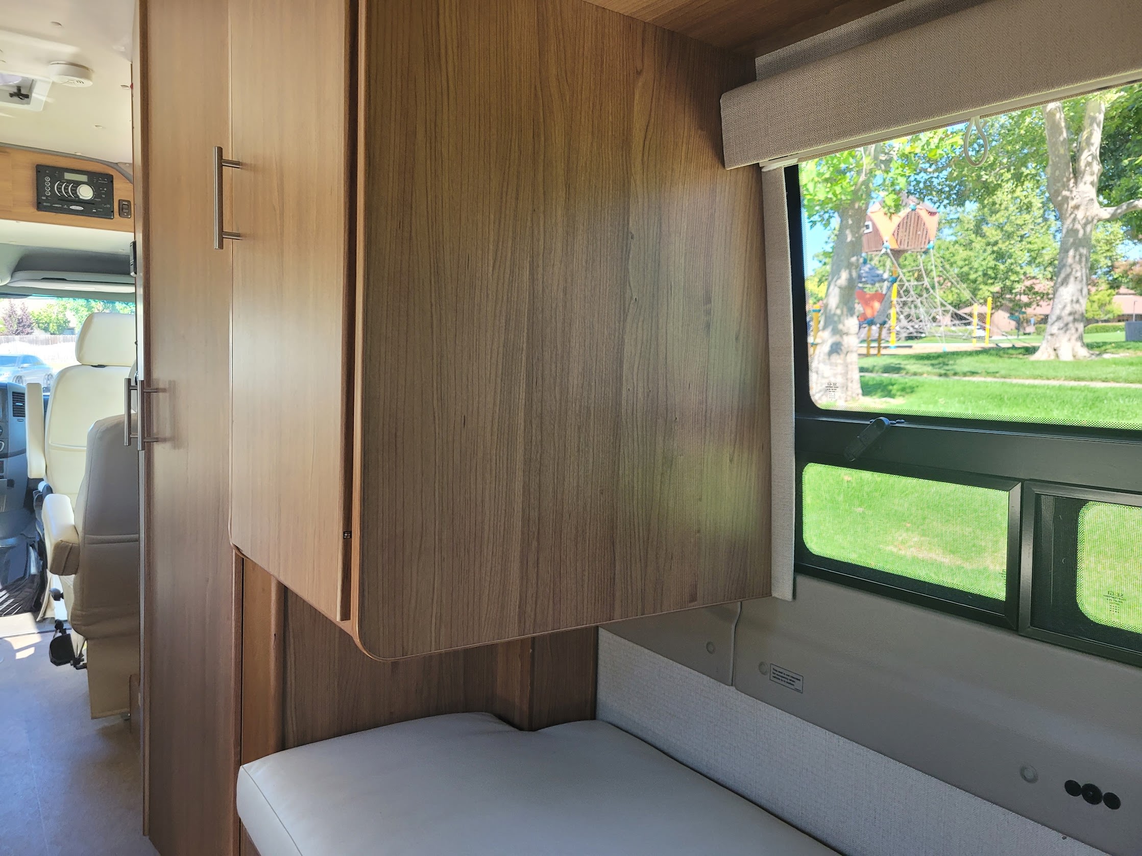 RV rental interior featuring wooden cabinets, cushioned seating, and a window view of a vibrant park playground.. Winnebago Era 2016