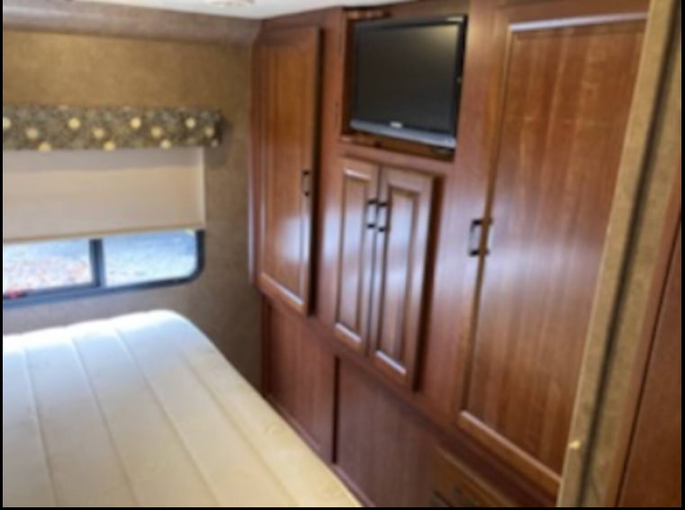 RV rental bedroom featuring a mattress, window with blinds, and built-in wooden cabinets with a mounted TV.. Forest River Forester 2016