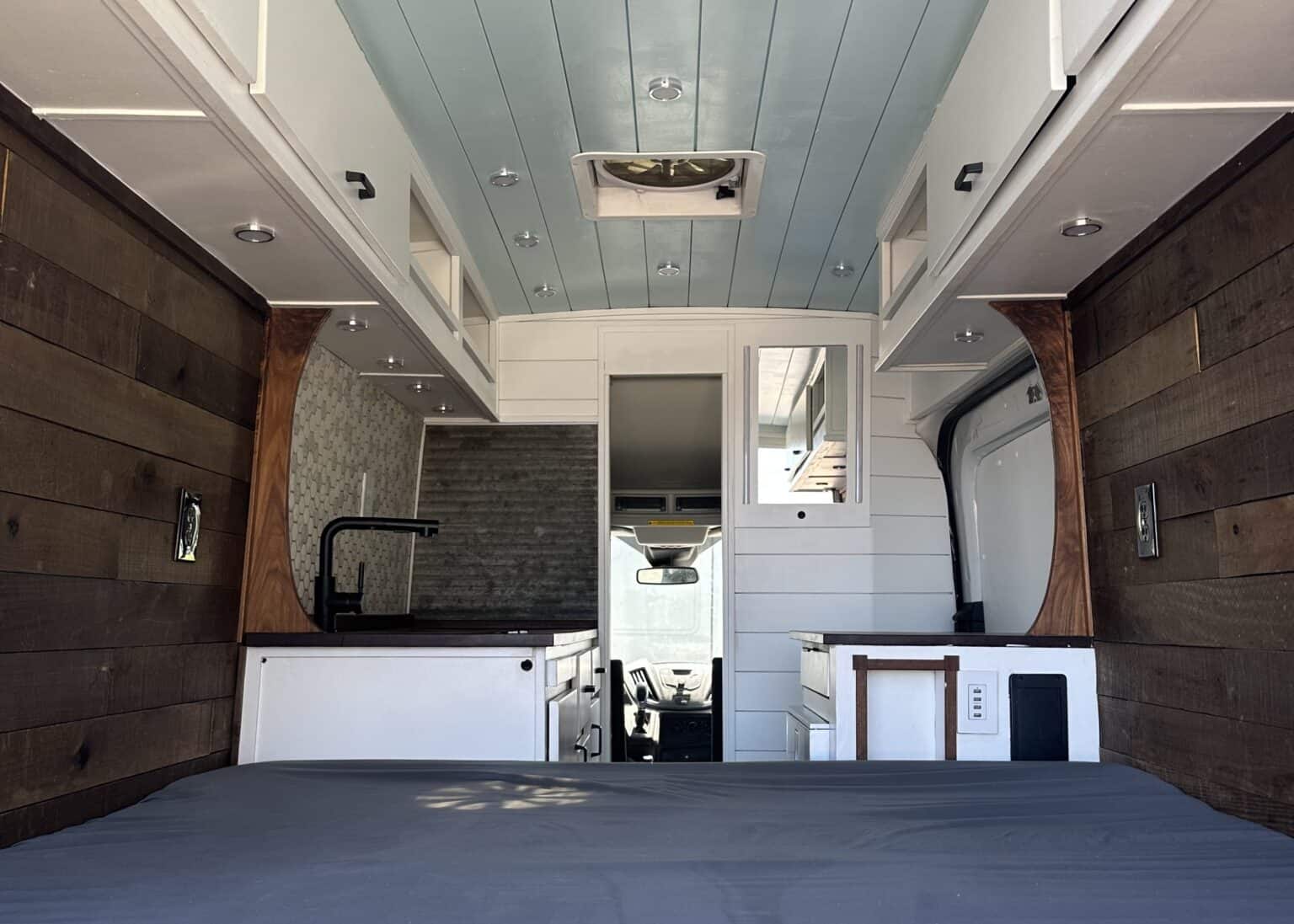An RV rental van's modern rustic interior showcasing a bed, kitchen, and ample storage, ideal for adventure.. Ford Transit 2017