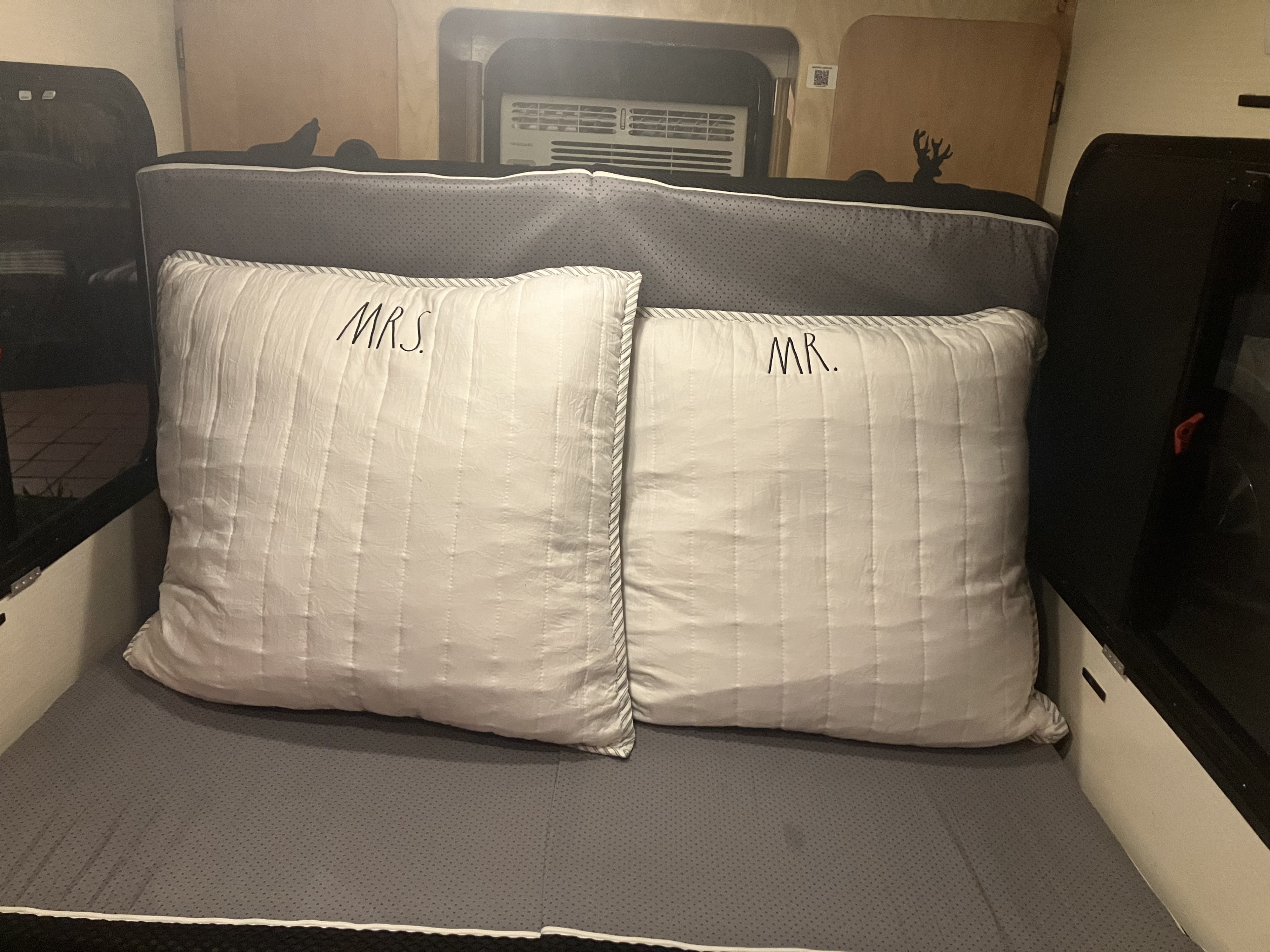 Comfortable RV rental bed with 'MR.' and 'MRS.' pillows, featuring a compact interior and AC unit.. Calmarc Panther 2016