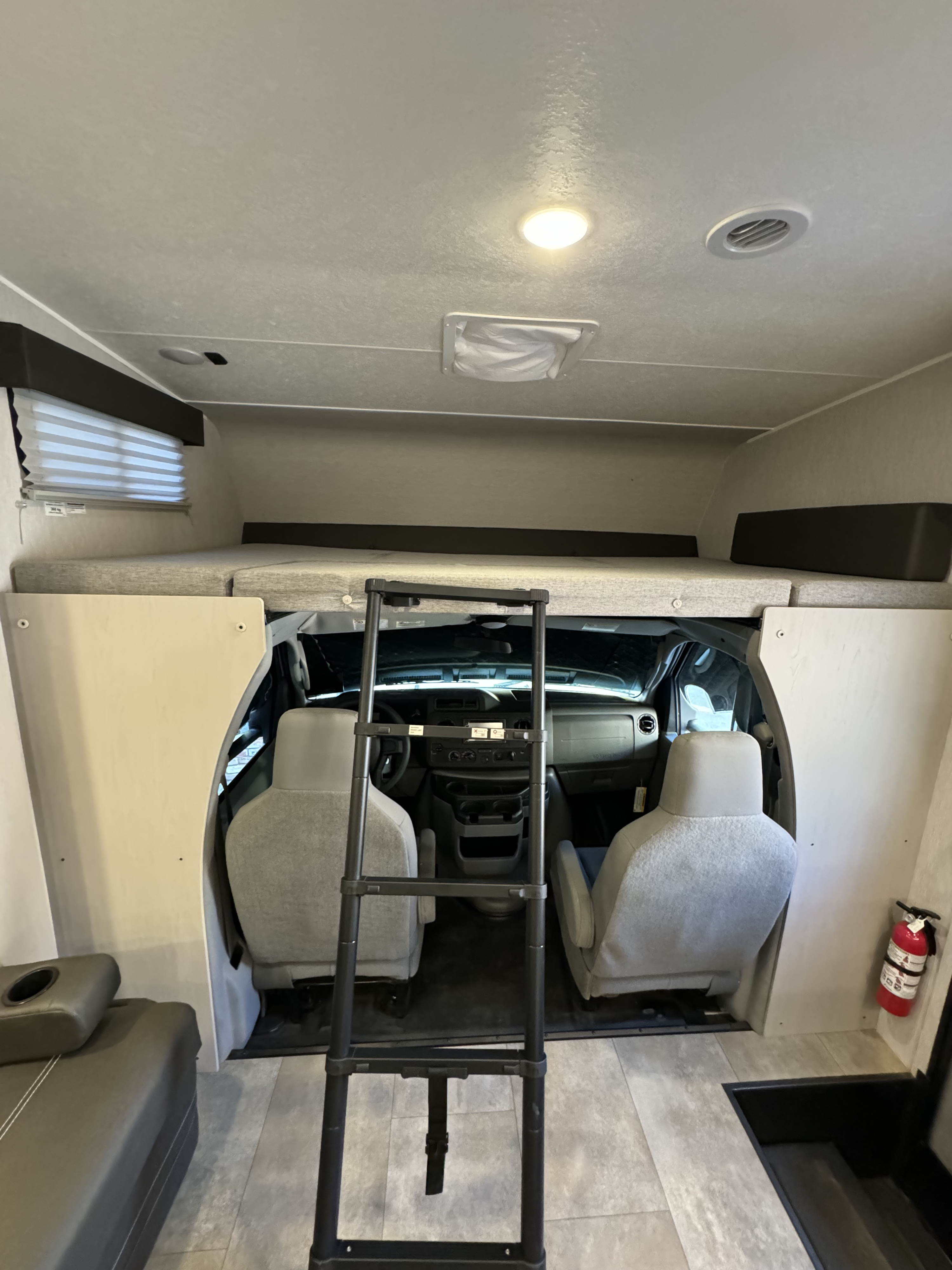 View inside an RV rental, highlighting the over-cab bunk with ladder access and vehicle's front cockpit area.. Forest River Coachmen Freelander 2023