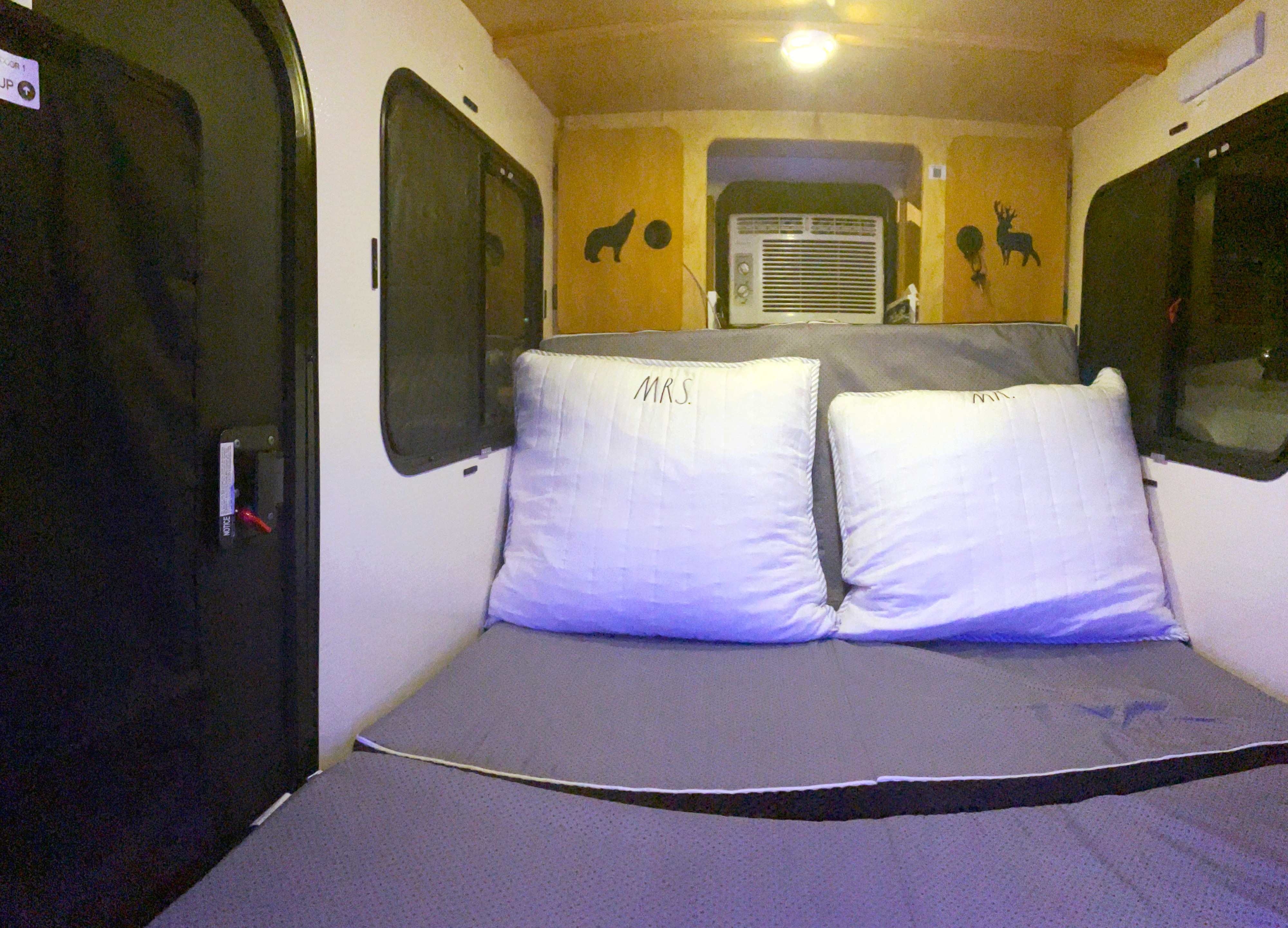 This RV rental's cozy bedroom features a bed with 'MRS.' and 'MR.' pillows, window AC unit, and wildlife decals.. Calmarc Panther 2016