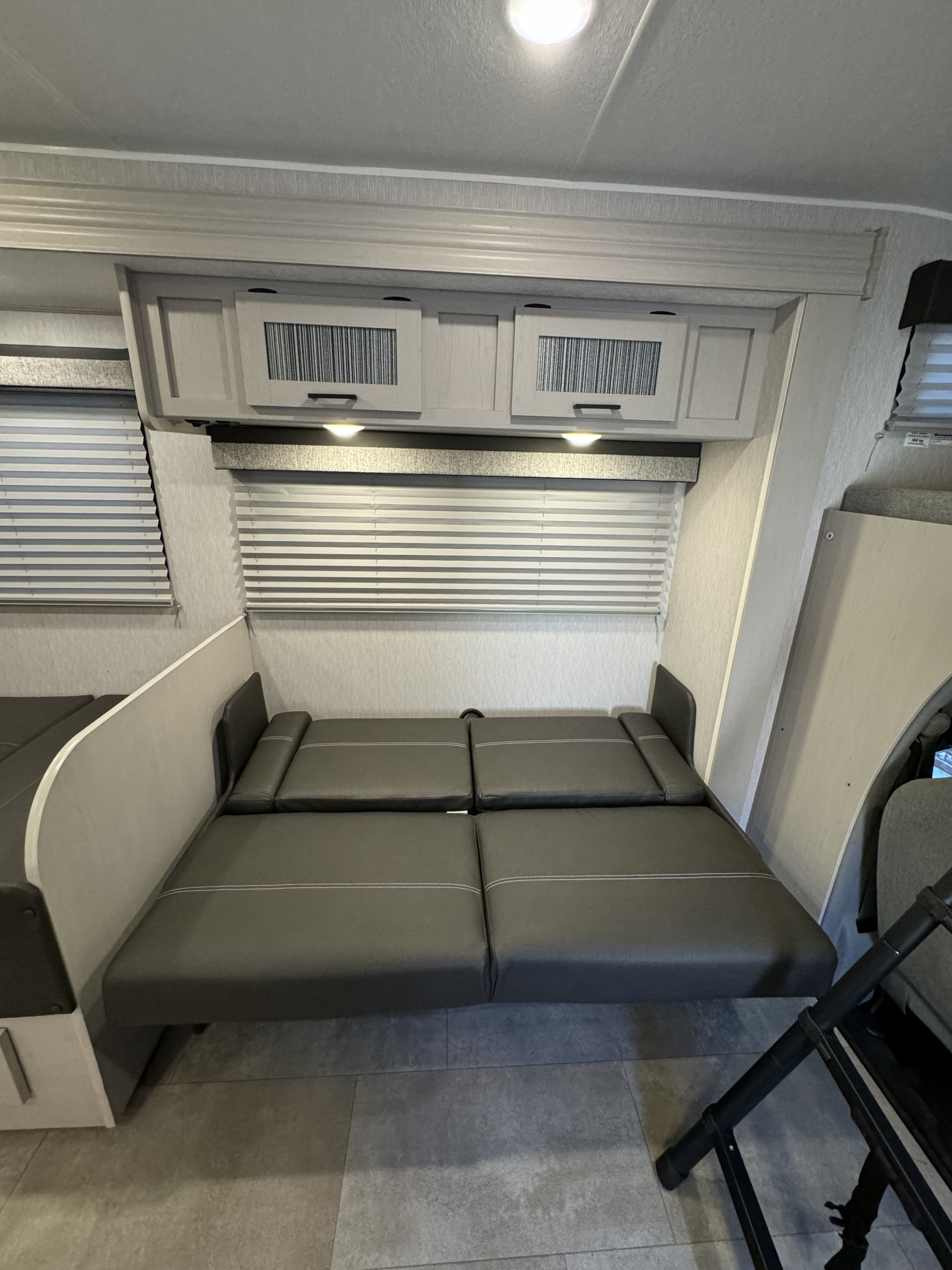 RV rental interior: A gray convertible sofa bed, overhead cabinets, window blinds, and gray floor tiling.. Forest River Coachmen Freelander 2023