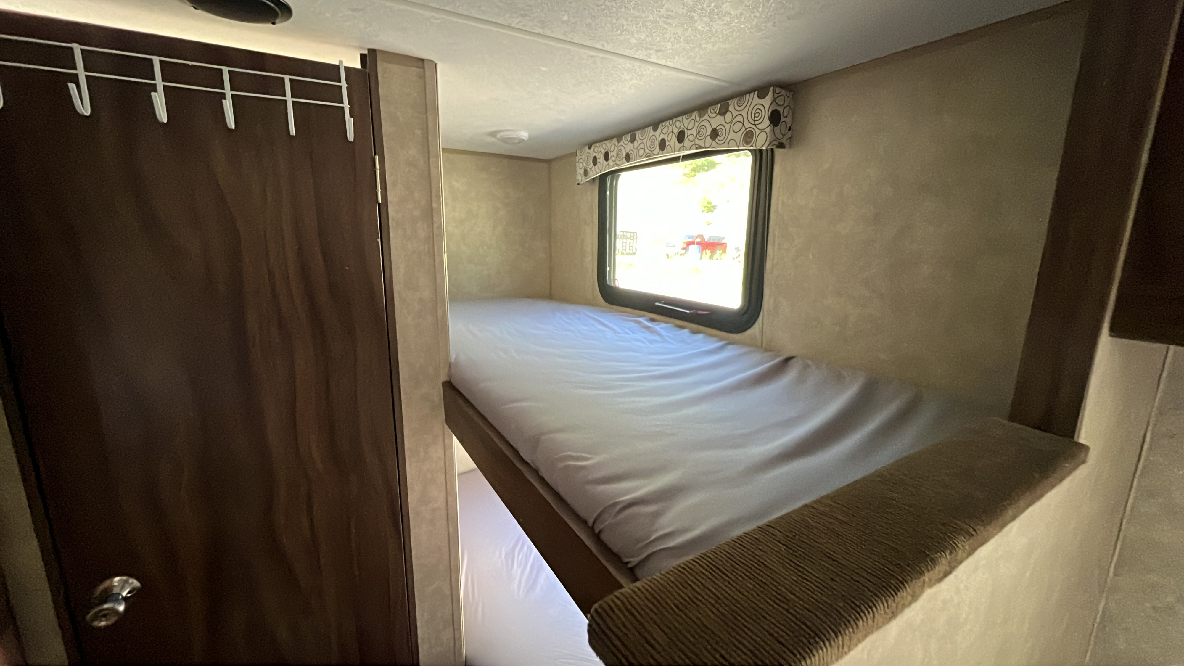 Inside an RV rental: A cozy top bunk bed with a window, a peek at the lower bunk, and a door with hooks on the left.. Clipper Clipper Trailer 2016