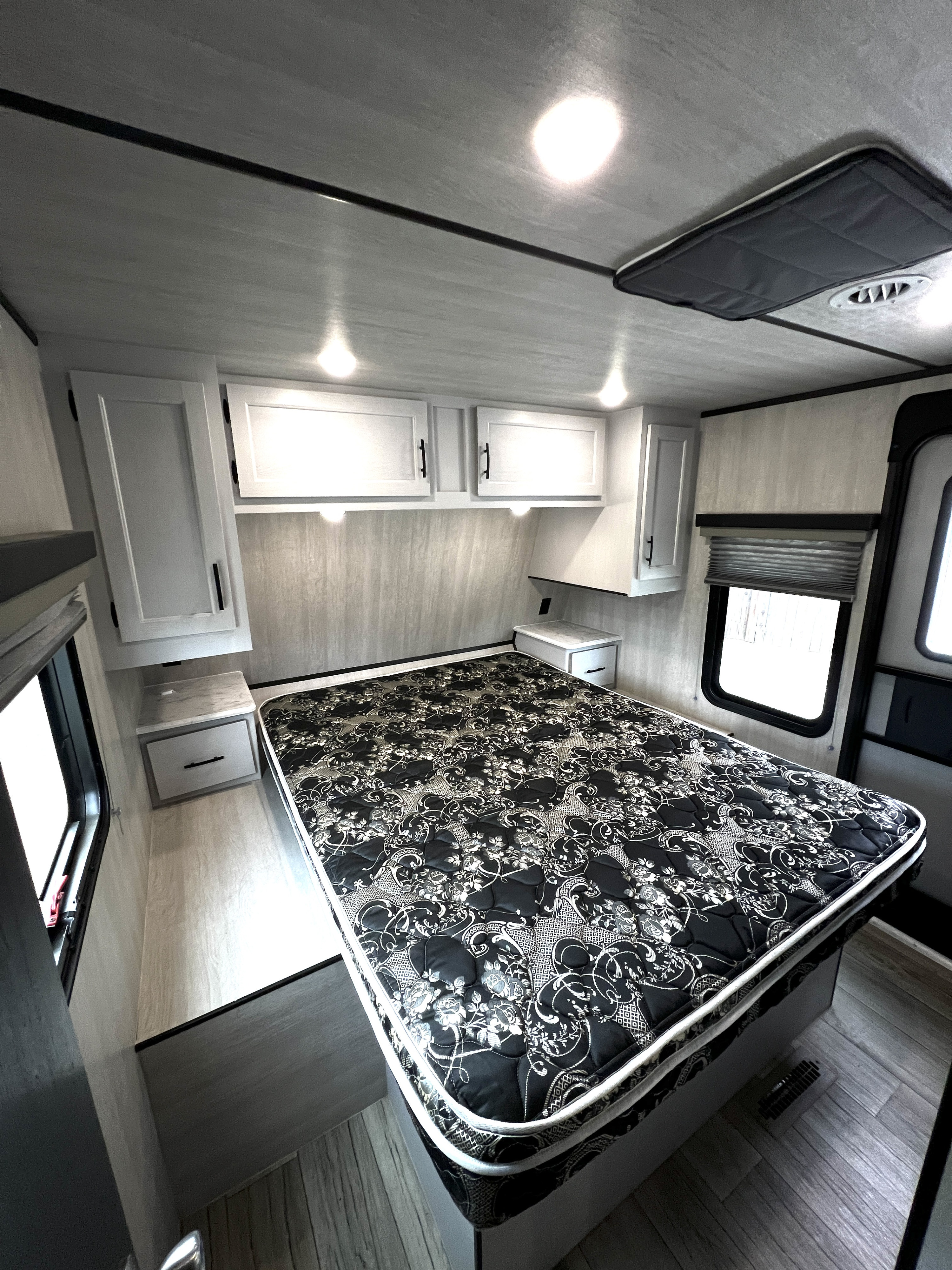 RV rental bedroom featuring a patterned bed, white overhead cabinets, and compact side tables in a brightly lit interior.. Genesis Supreme 27RLS 2024