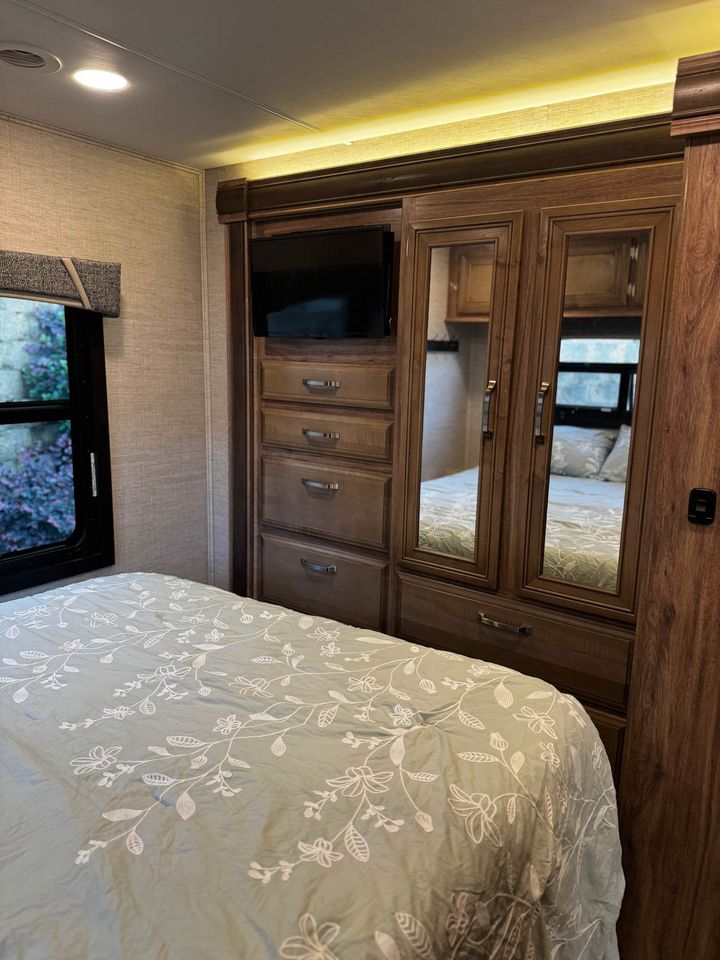 Cozy RV rental bedroom with a floral bedspread, built-in storage, TV, and mirrored closet.. Jayco Greyhawk 2021
