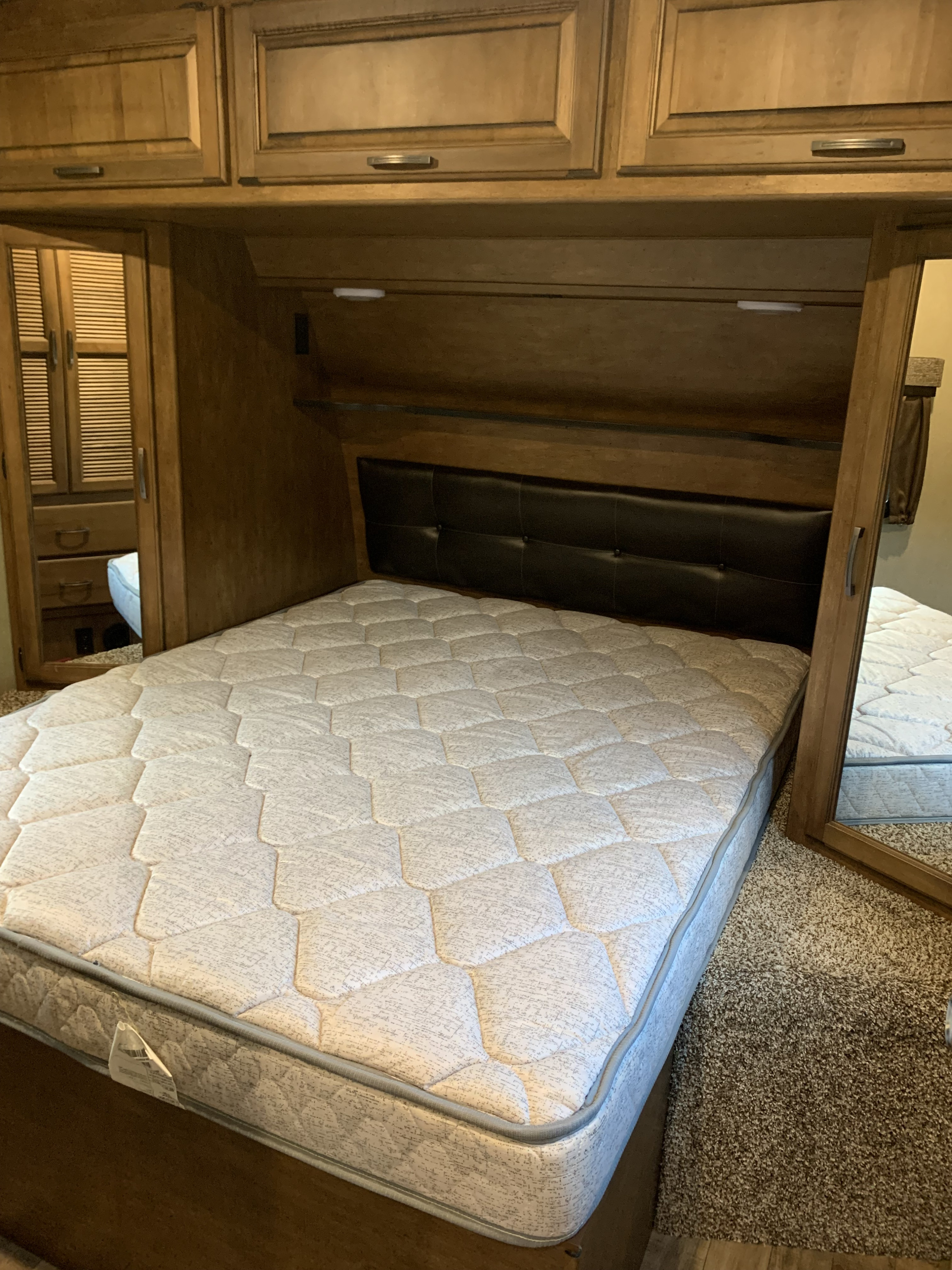 Explore this clean RV rental bedroom featuring a comfortable bed, overhead cabinets, and spacious mirrored closets.. Reflection BHT33 2018