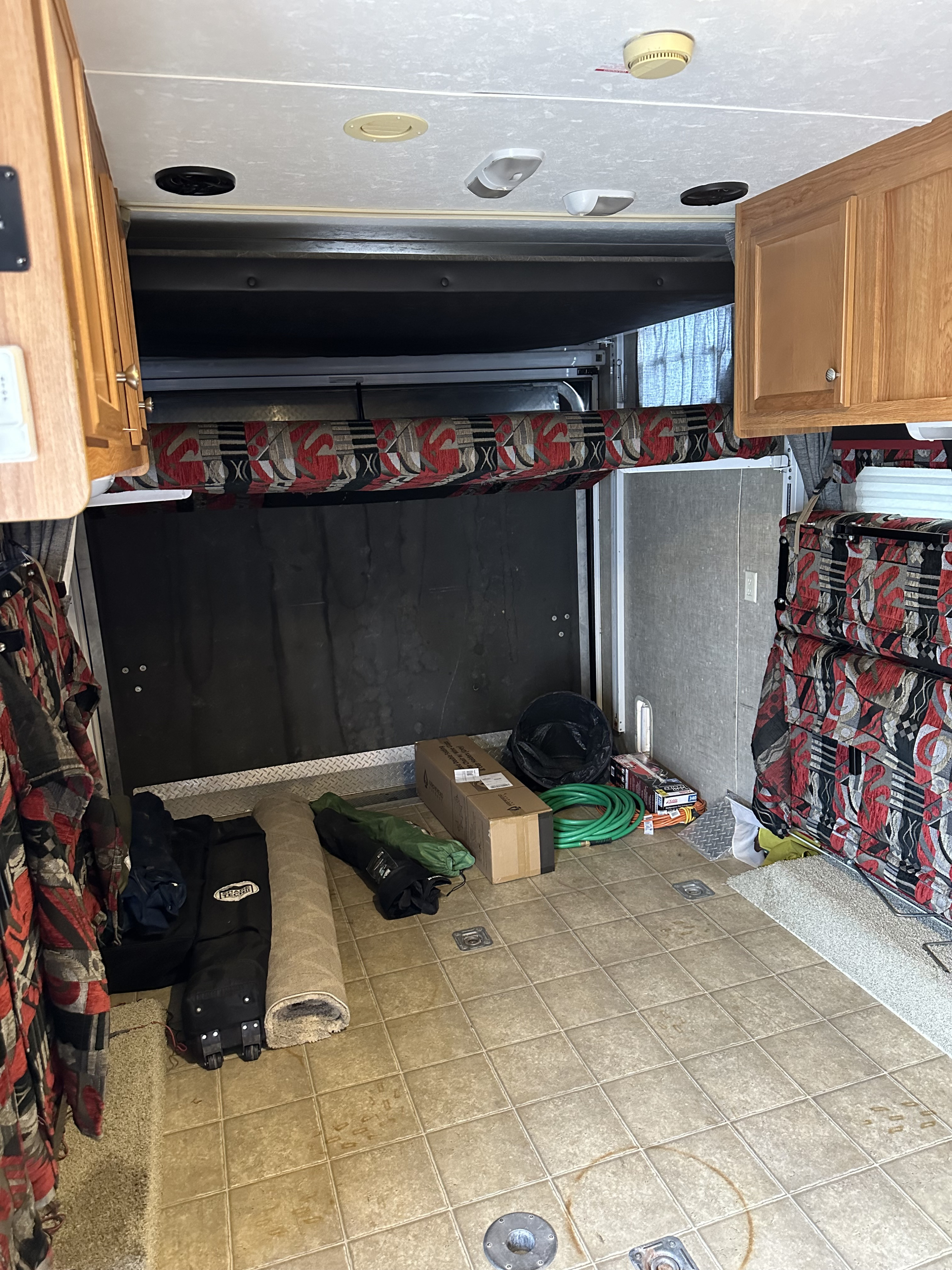 RV rental toy hauler interior: a versatile cargo space with a raised bunk bed, wood cabinets, and gear on a tiled floor.. Jayco Octane 2008