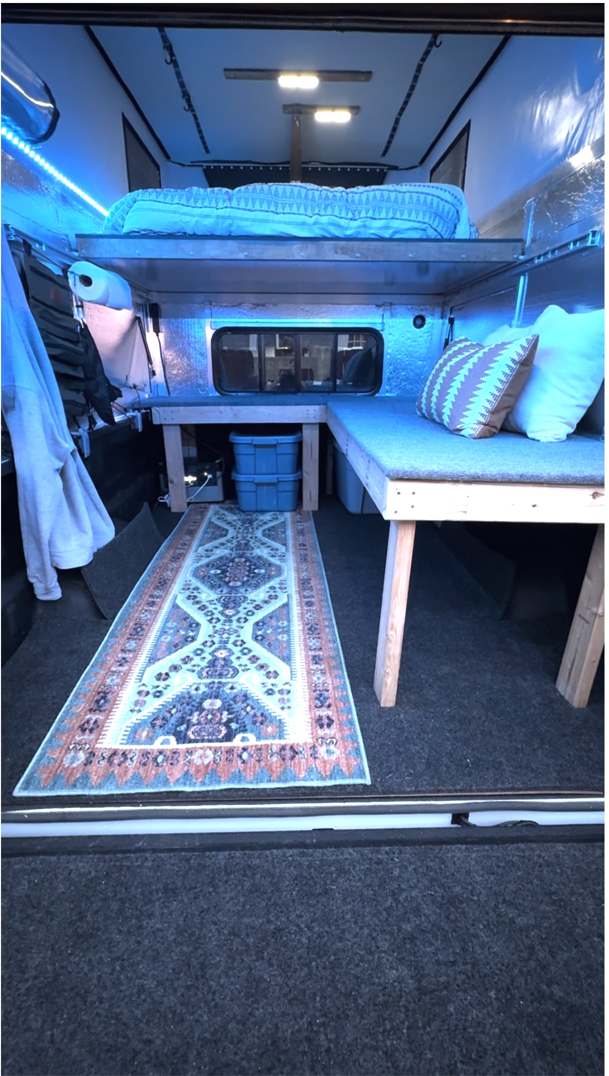 Cozy RV rental: this camper interior features a raised bed, seating, storage, and blue ambient lighting.. Toyota Tundra 2021