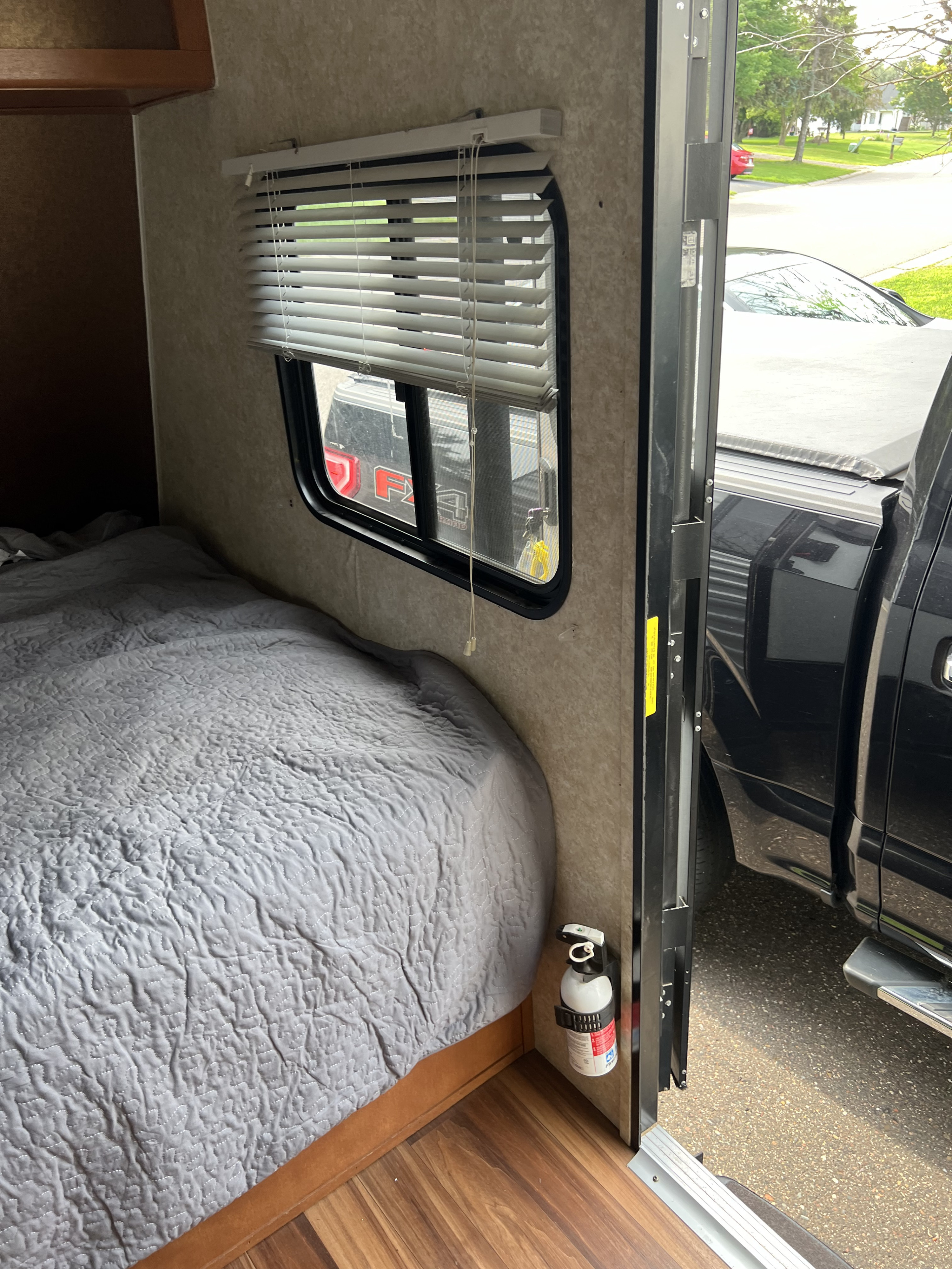 RV rental interior with a cozy bed, window views, and a visible fire extinguisher for safety near the open door.. Gulf Stream Ameri-Lite 2018