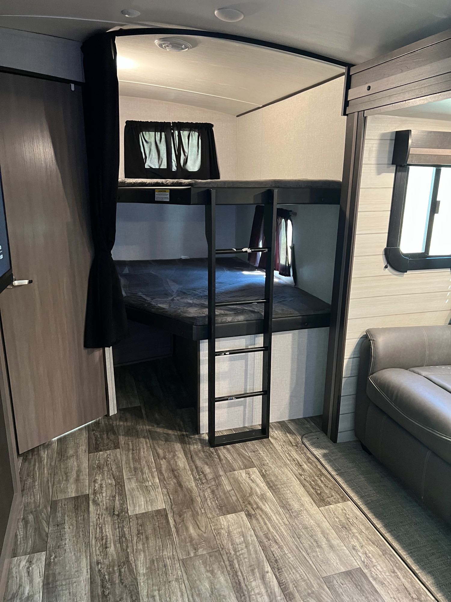 RV rental interior: A functional bunk bed area with ladder, privacy curtain, and modern wood-look flooring, great for travel.. Crossroads RV Sunset Trail Super Lite 2022