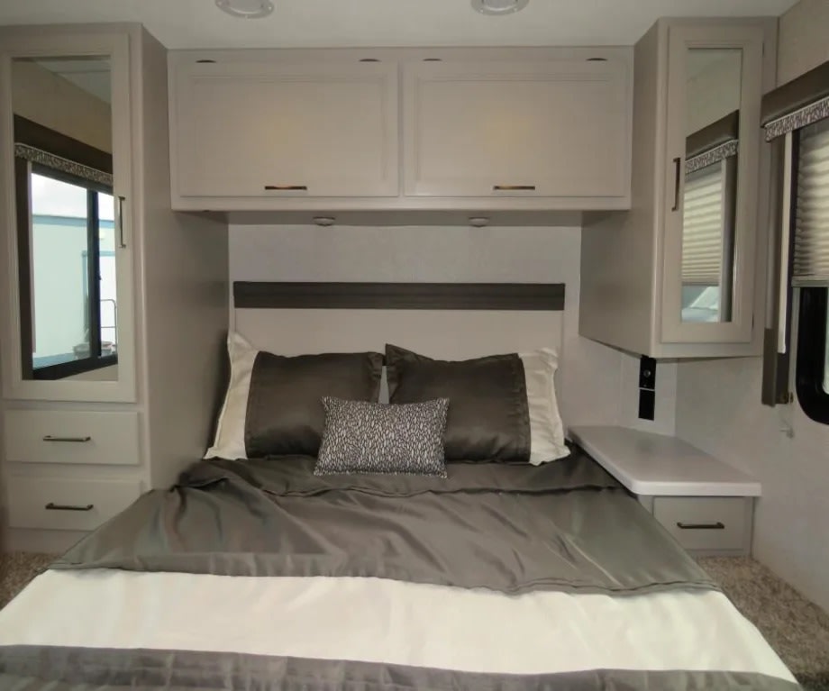 This cozy RV rental bedroom features a comfy bed, overhead cabinets, and mirrored wardrobes for smart storage, perfect for travel.. Thor Quantum 2023