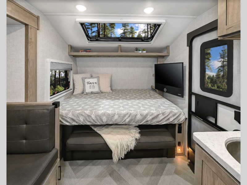 Compact rv rental living space with a pull-down bed over a sofa, TV, small kitchen, and large windows.. Ember MDB 2023