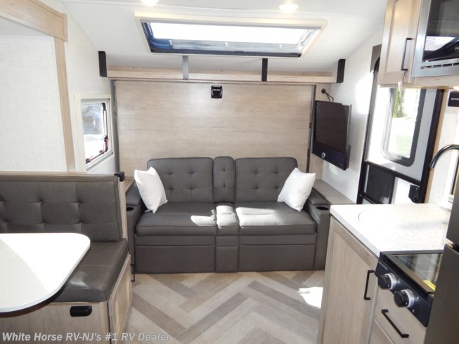 RV rental interior with a gray sofa, wall-mounted TV, kitchen area, and dinette. A compact living space with a skylight.. Ember MDB 2023