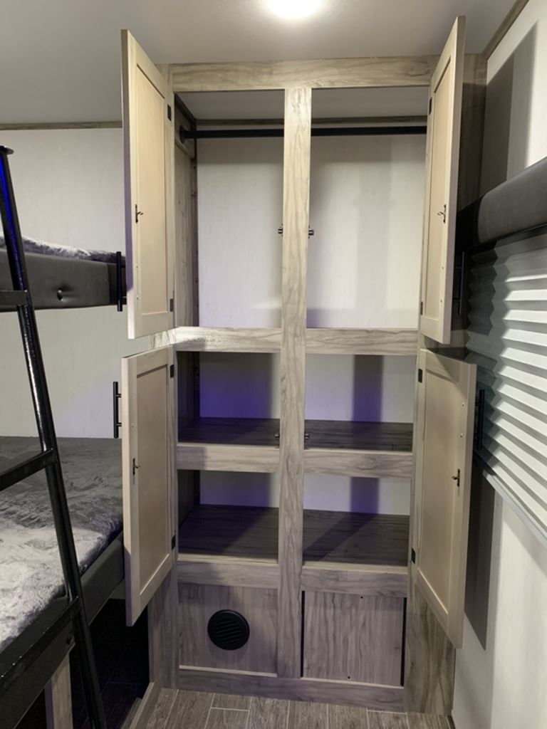 RV rental interior features an open wardrobe with shelving and hanging space, plus cozy bunk beds.. Forest River Alpha Wolf 2022