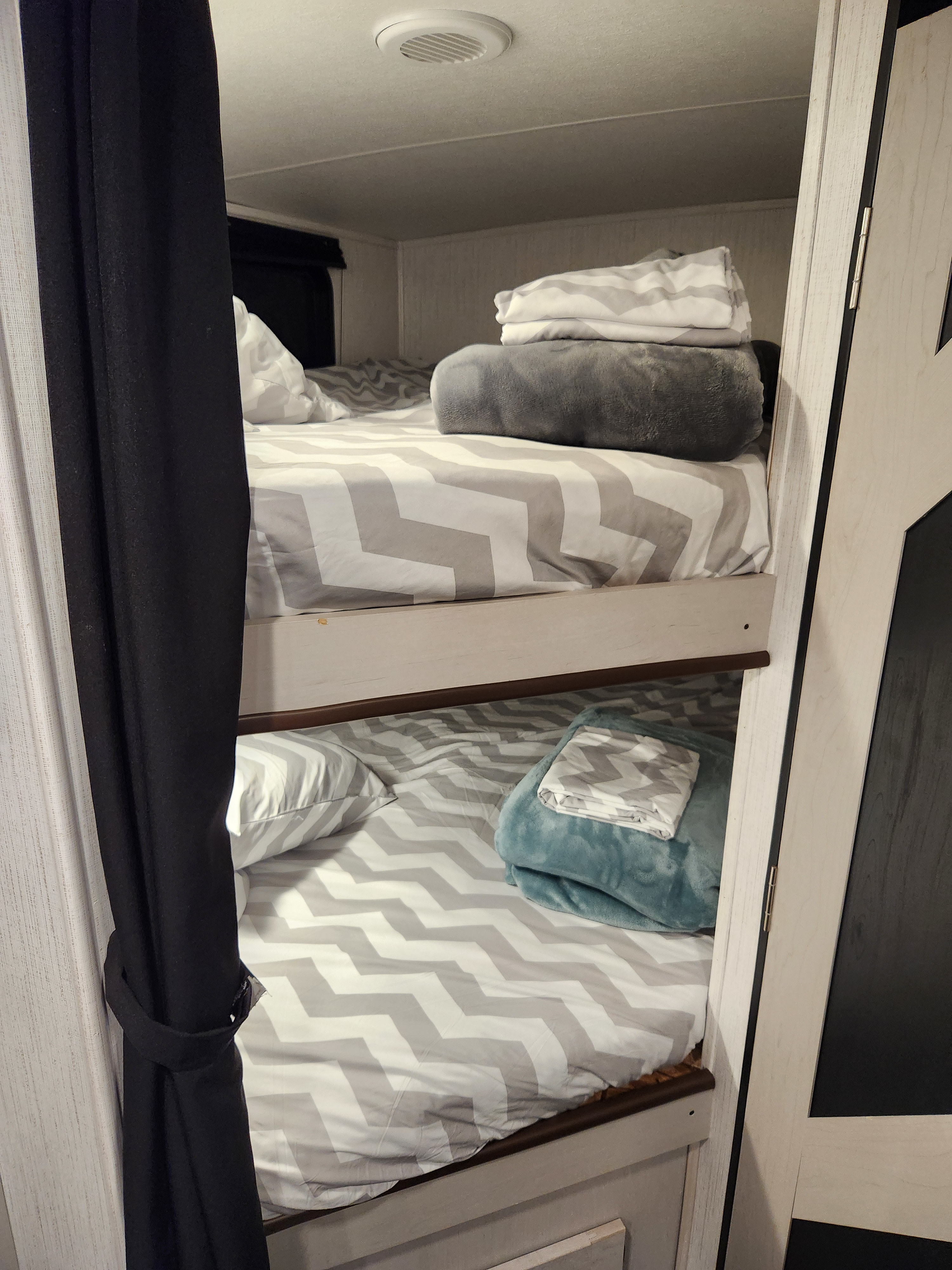Cozy RV rental bunk beds feature stylish chevron bedding and blankets, offering a comfortable sleeping space for your next adventure.. Heartland Mallard 2022