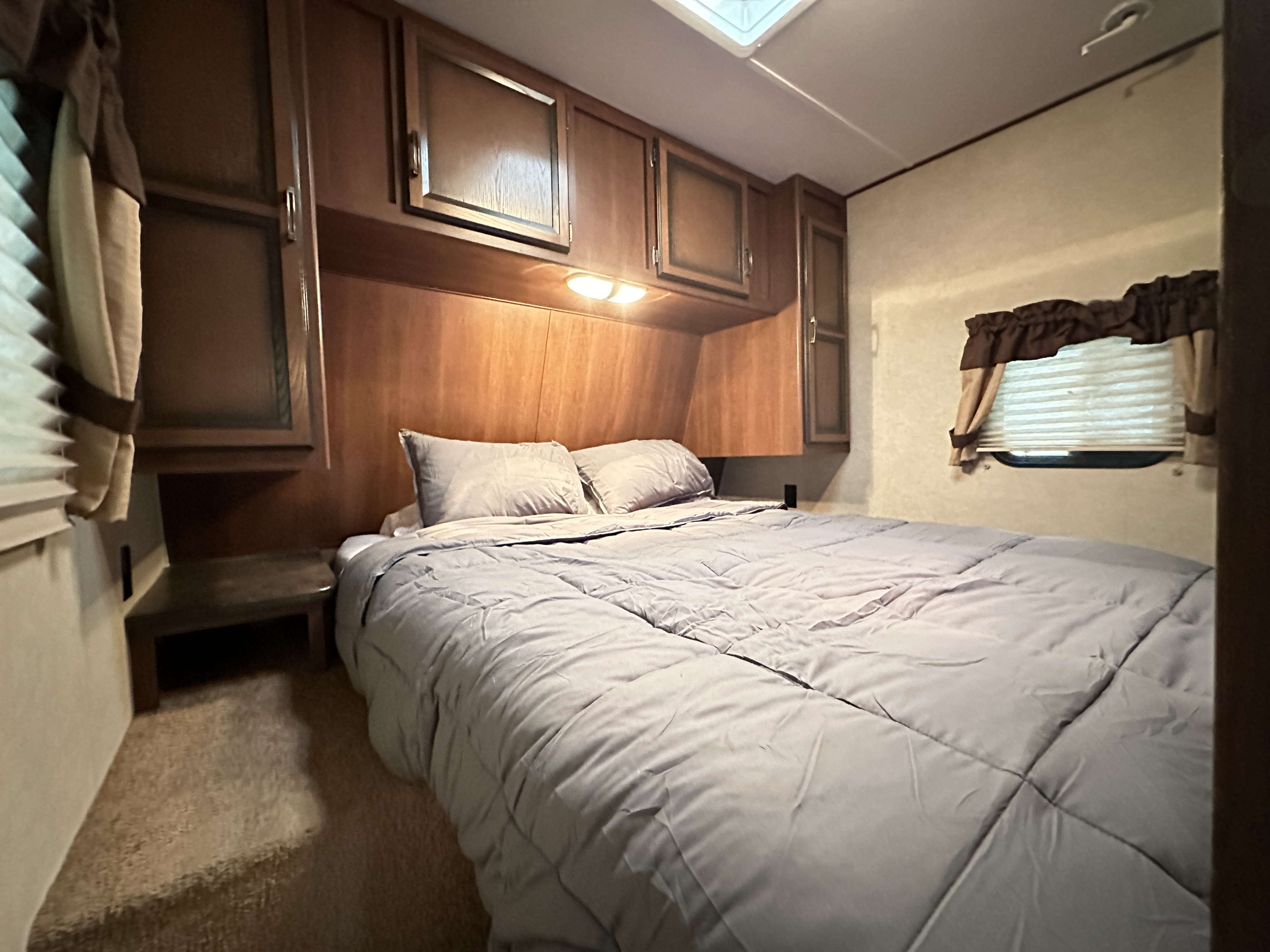 Cozy rv rental bedroom: a large bed with gray bedding, wooden overhead cabinets, and a window. Perfect for comfortable stays.. Crossroads RV Zinger 2012