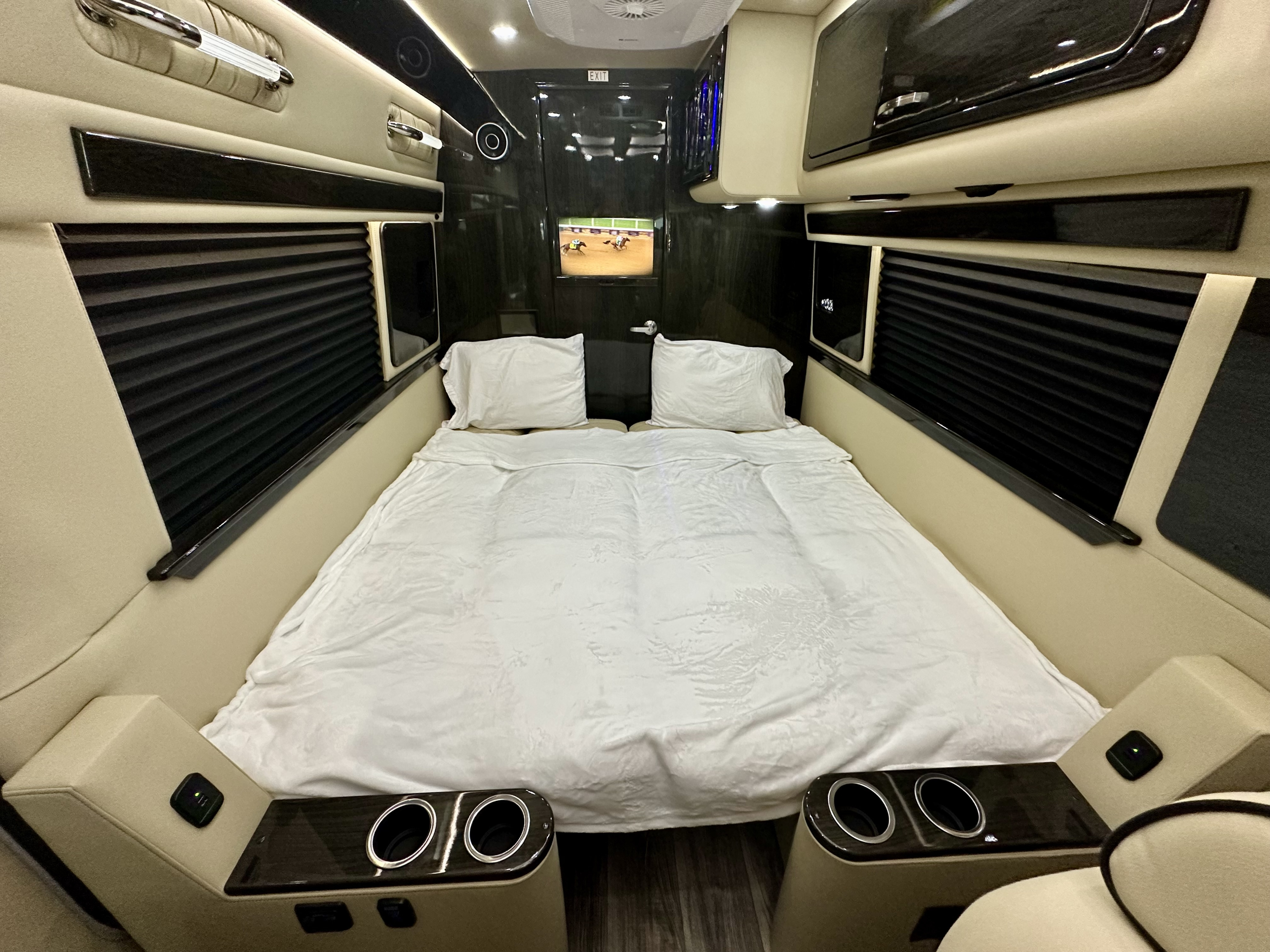 Interior of a luxury RV rental featuring a large bed with white bedding, TV, built-in cup holders, and pleated window blinds.. Ultimate Toys Ultimate RV 2025