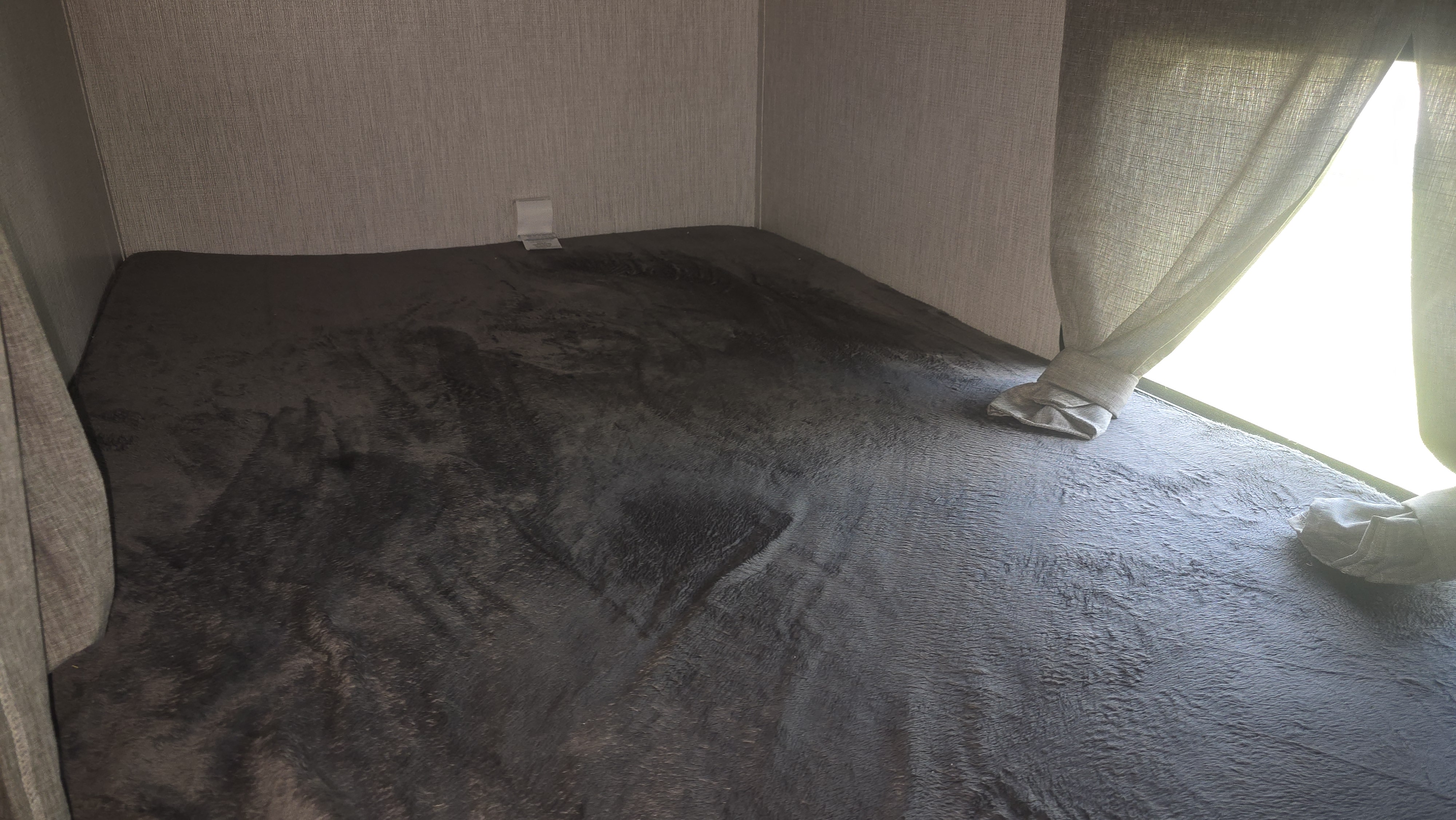 RV rental bunk: Dark gray plush bed, textured walls, and a bright window with tied curtains.. Palomino Solaire 2022