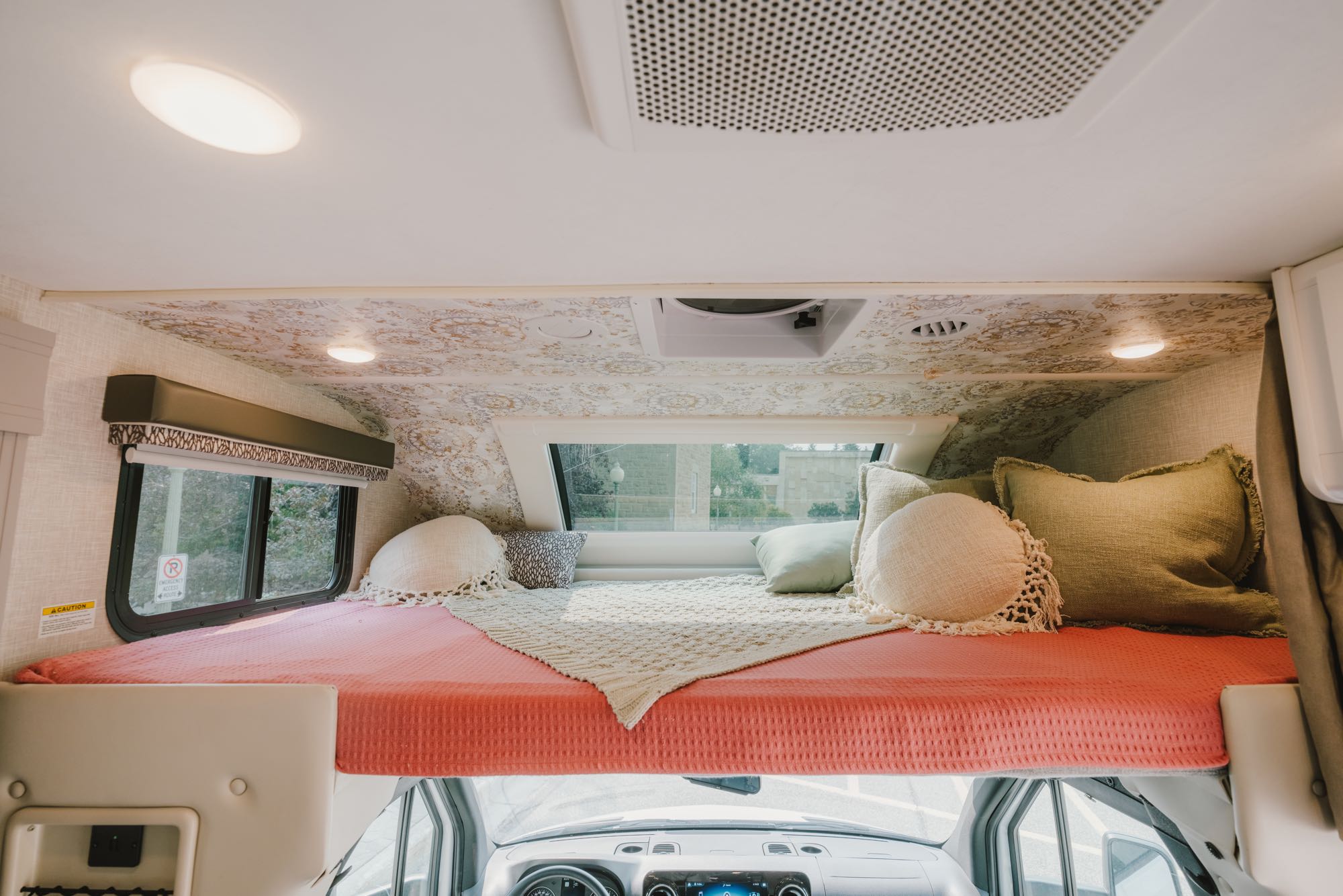 This RV rental's cozy cab-over bunk features a coral bed, decorative pillows, patterned ceiling, and large windows.. Thor Echelon 2024