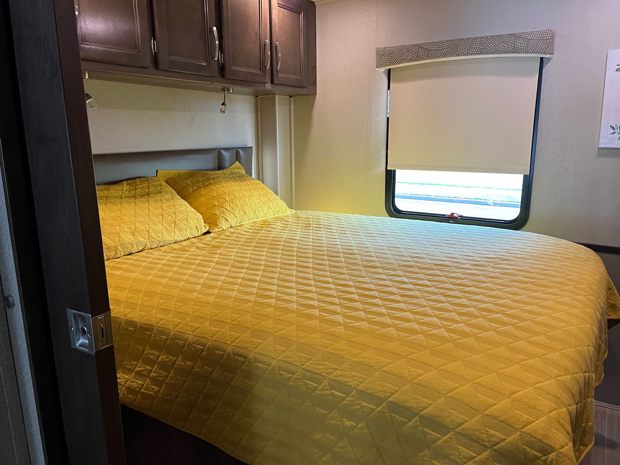 Comfortable RV rental bedroom featuring a sunny yellow quilted bed, overhead cabinets, and window. Ideal for travel.. Entegra Coach Vision 2020