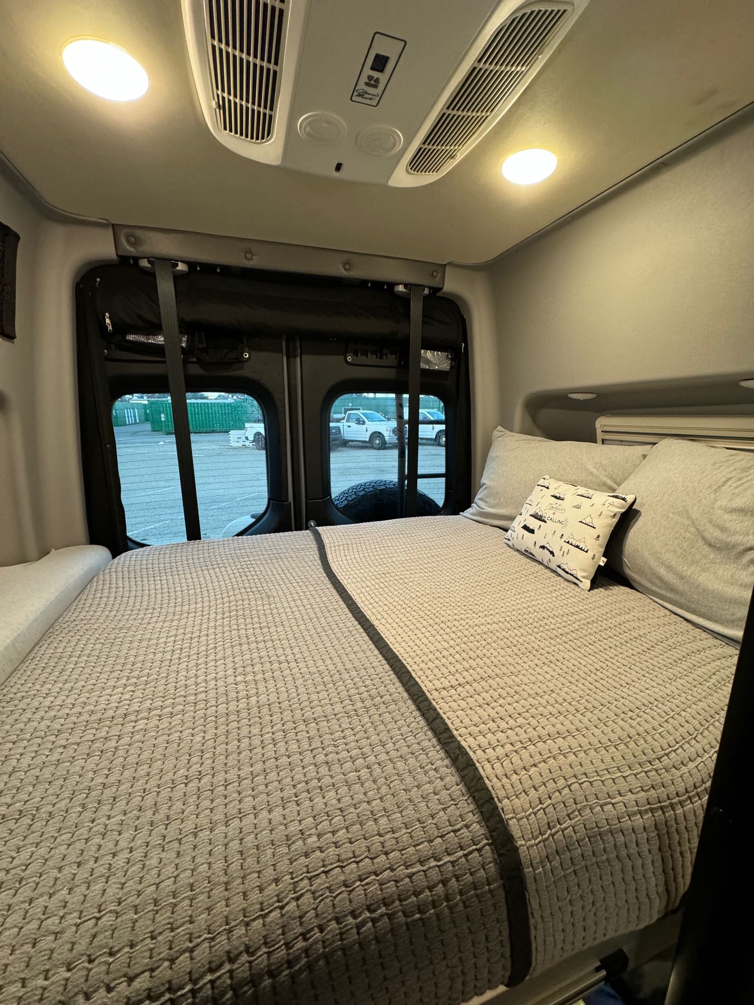 Cozy rv rental interior: bed with gray bedding, pillows & view out rear windows. Ideal sleeping area for adventure.. Winnebago Revel 2022