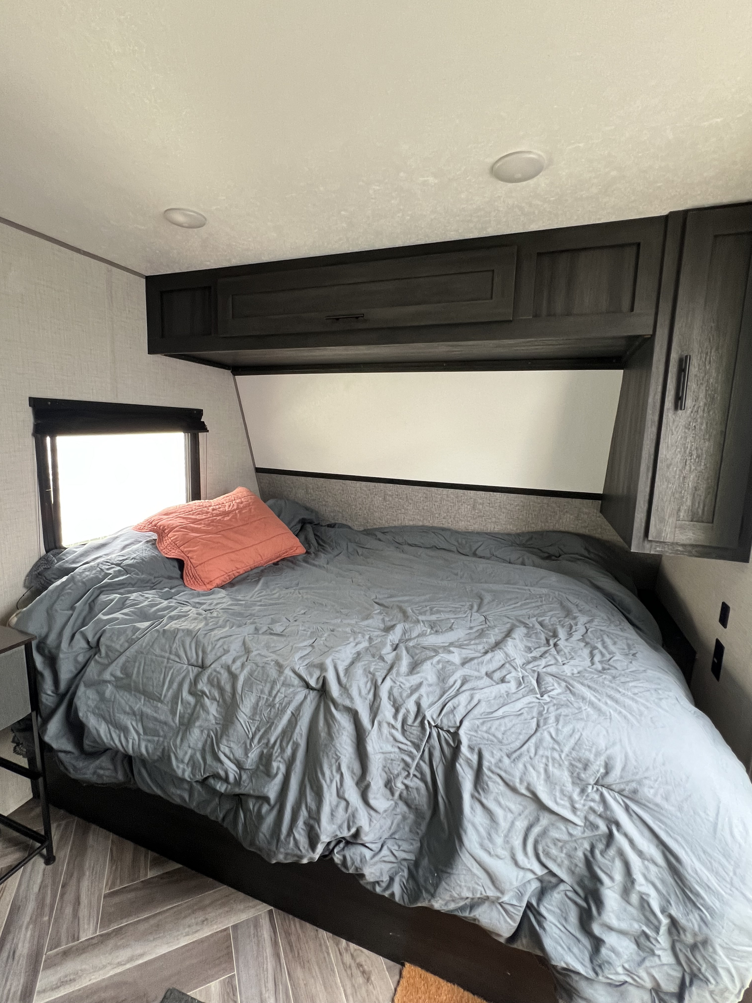 Cozy RV rental bedroom with a grey bed, dark overhead cabinets, and window for travel comfort.. Forest River Ozark 2021