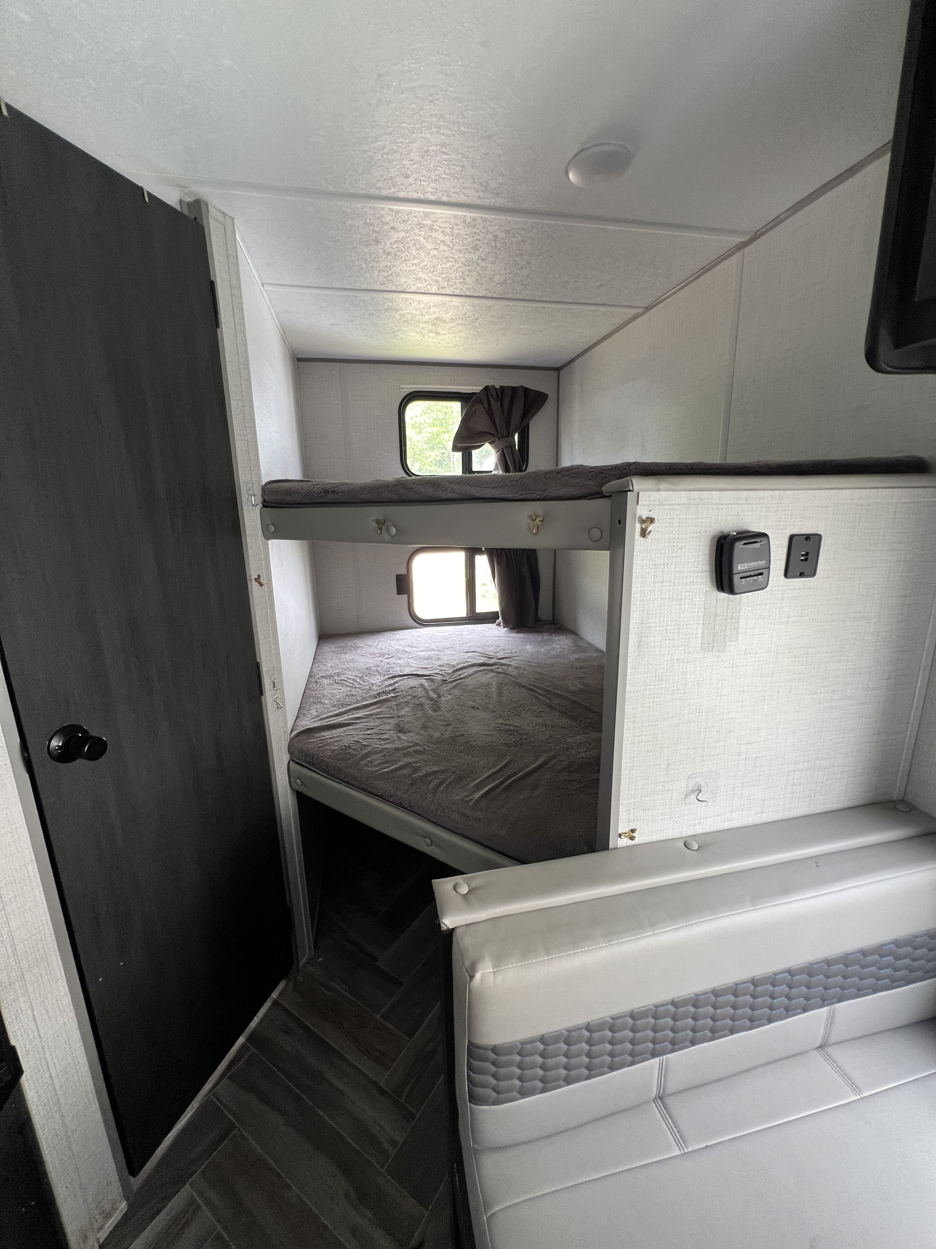 Modern RV rental interior with comfortable bunk beds, a dark door, and a light-colored seating area.. Forest River Ozark 2021