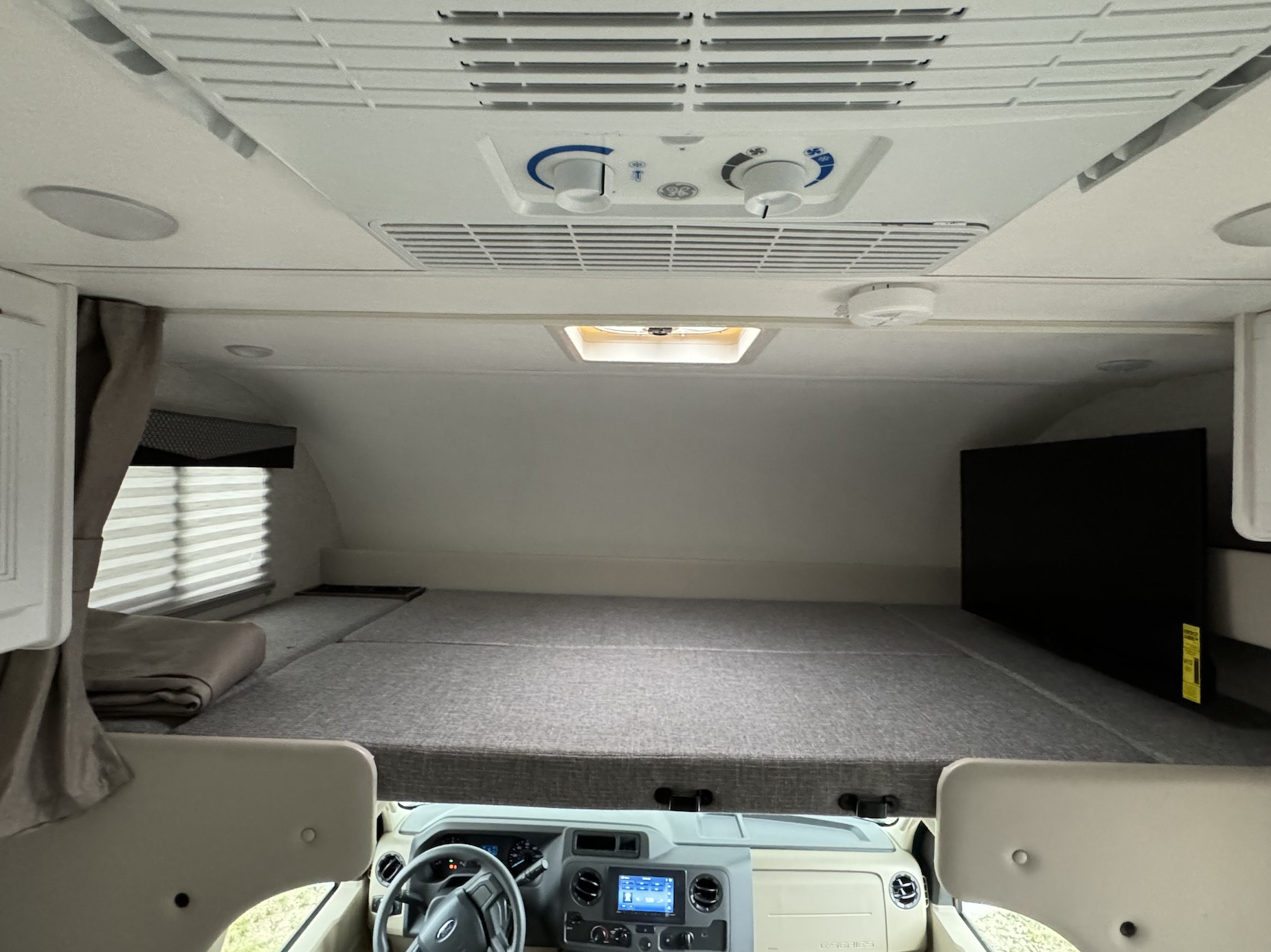 An rv rental's spacious overhead sleeping area, featuring a large bunk bed, AC unit, and TV. Ready for travel comfort.. Thor Motor Coach Freedom Elite 2024