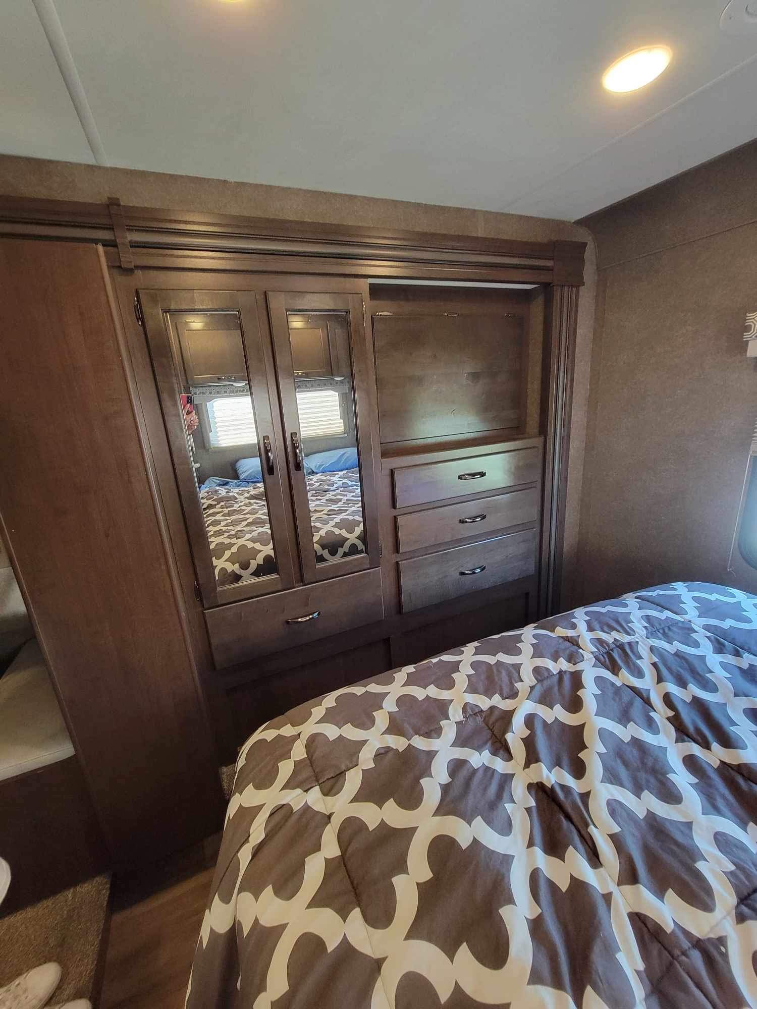 This RV rental bedroom features a comfy bed, mirrored wardrobe, and dresser, offering comfort and storage for your travels.. Thor Four Winds 2020