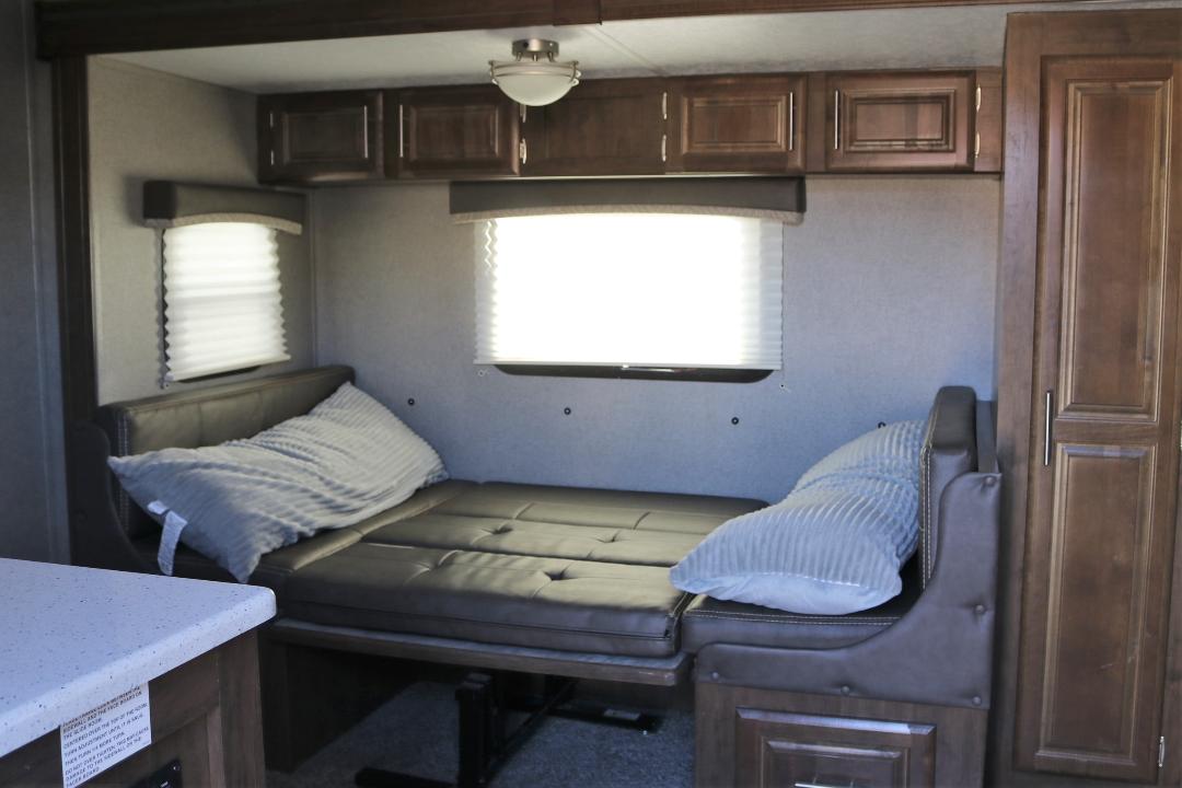 RV rental interior showing a dinette converted into a bed with pillows, alongside windows and overhead cabinets.. Forest River Rockwood Mini Lite 2019