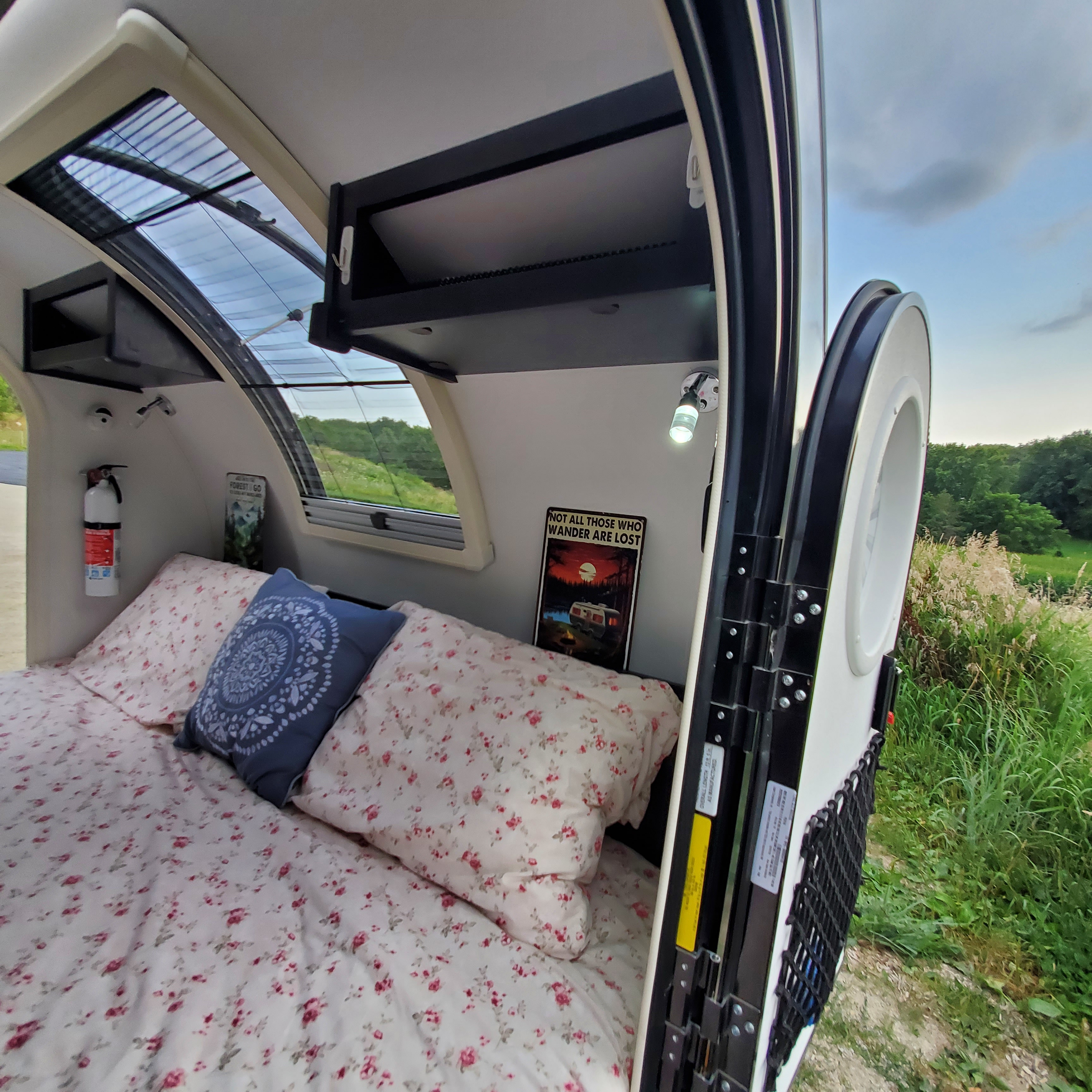Step inside this cozy RV rental camper, featuring a comfortable bed, overhead storage, and an open door to nature.. nuCamp T@G 2023