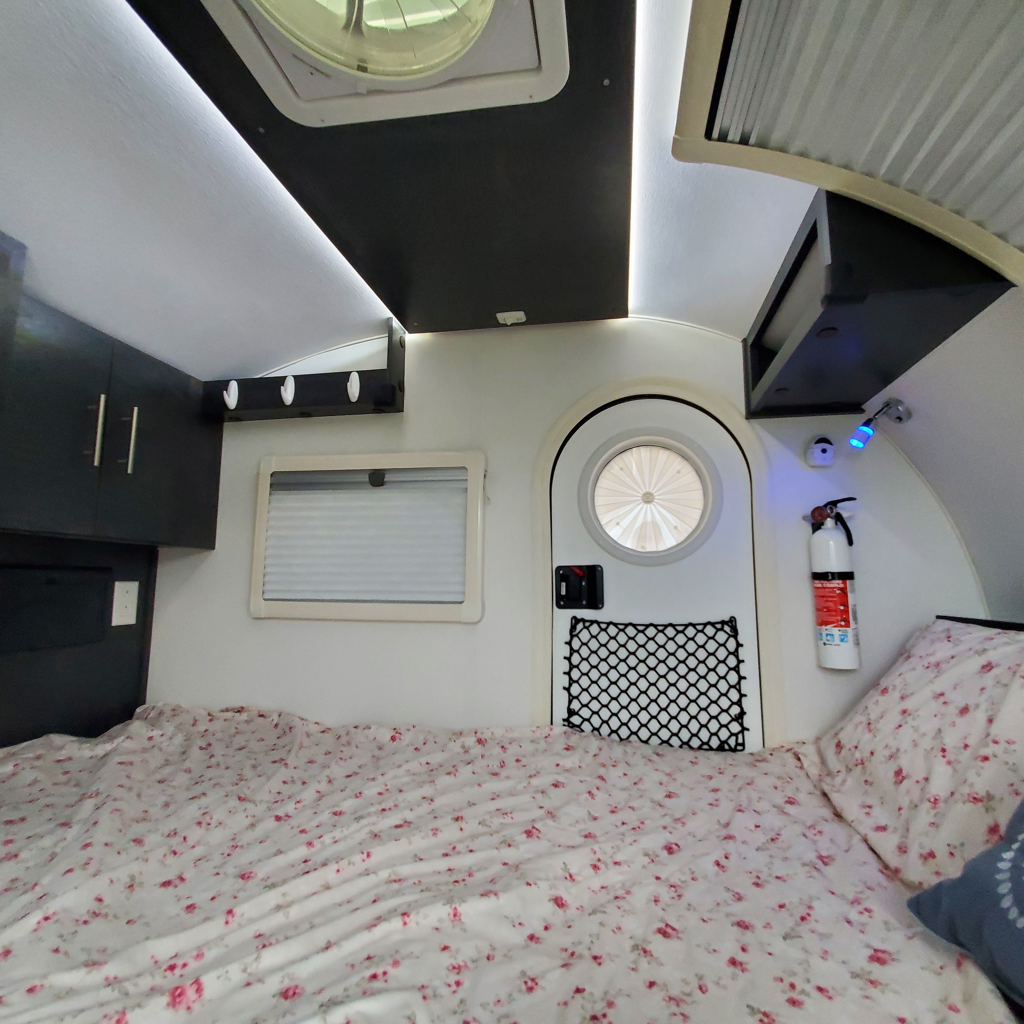 RV rental bedroom view: Floral bed, cabinets, and a unique round window create a cozy camper interior.. nuCamp T@G 2023