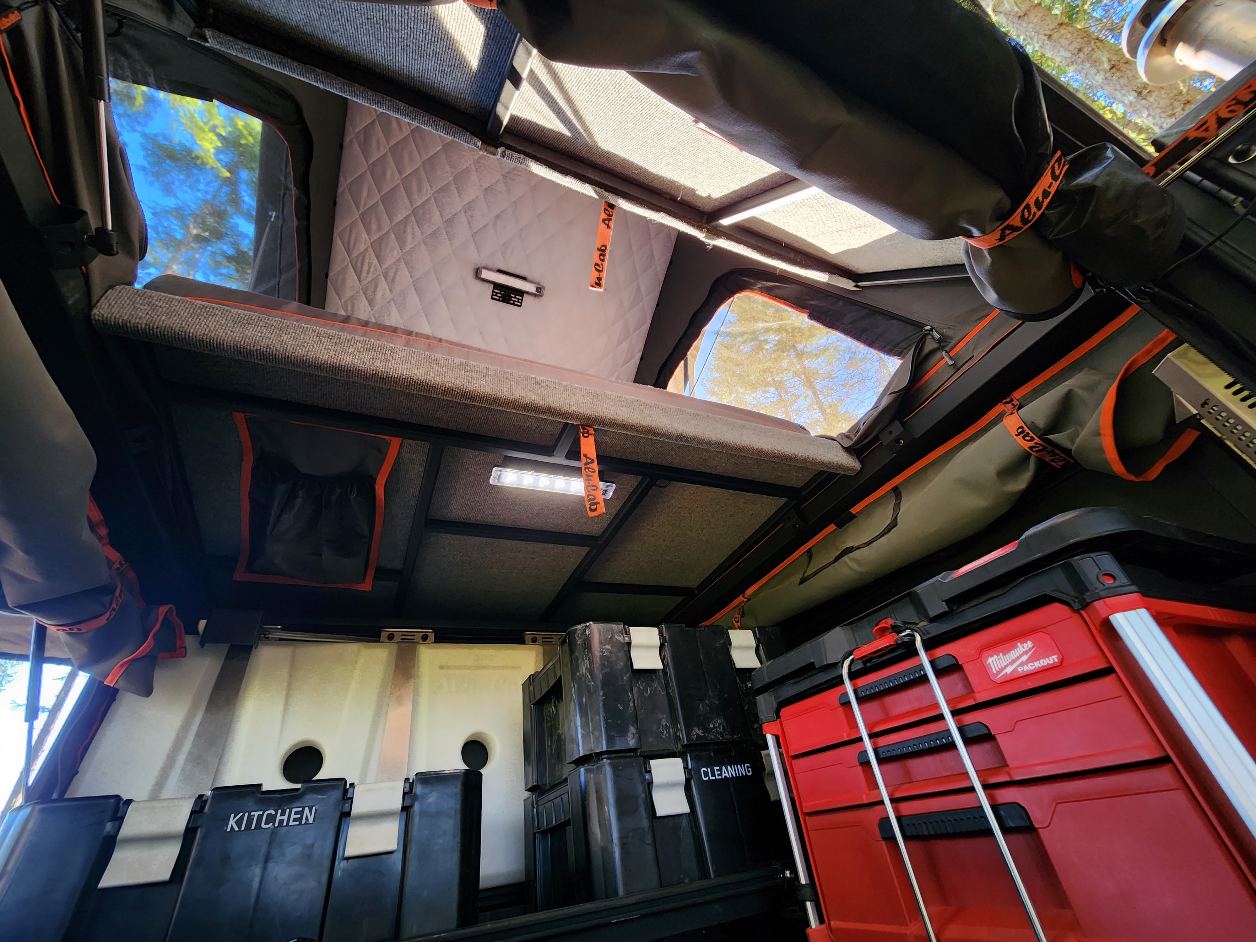 This RV rental-ready camper interior features a bed, organized storage for kitchen & cleaning, and Milwaukee PACKOUT.. Nissan Frontier 2022