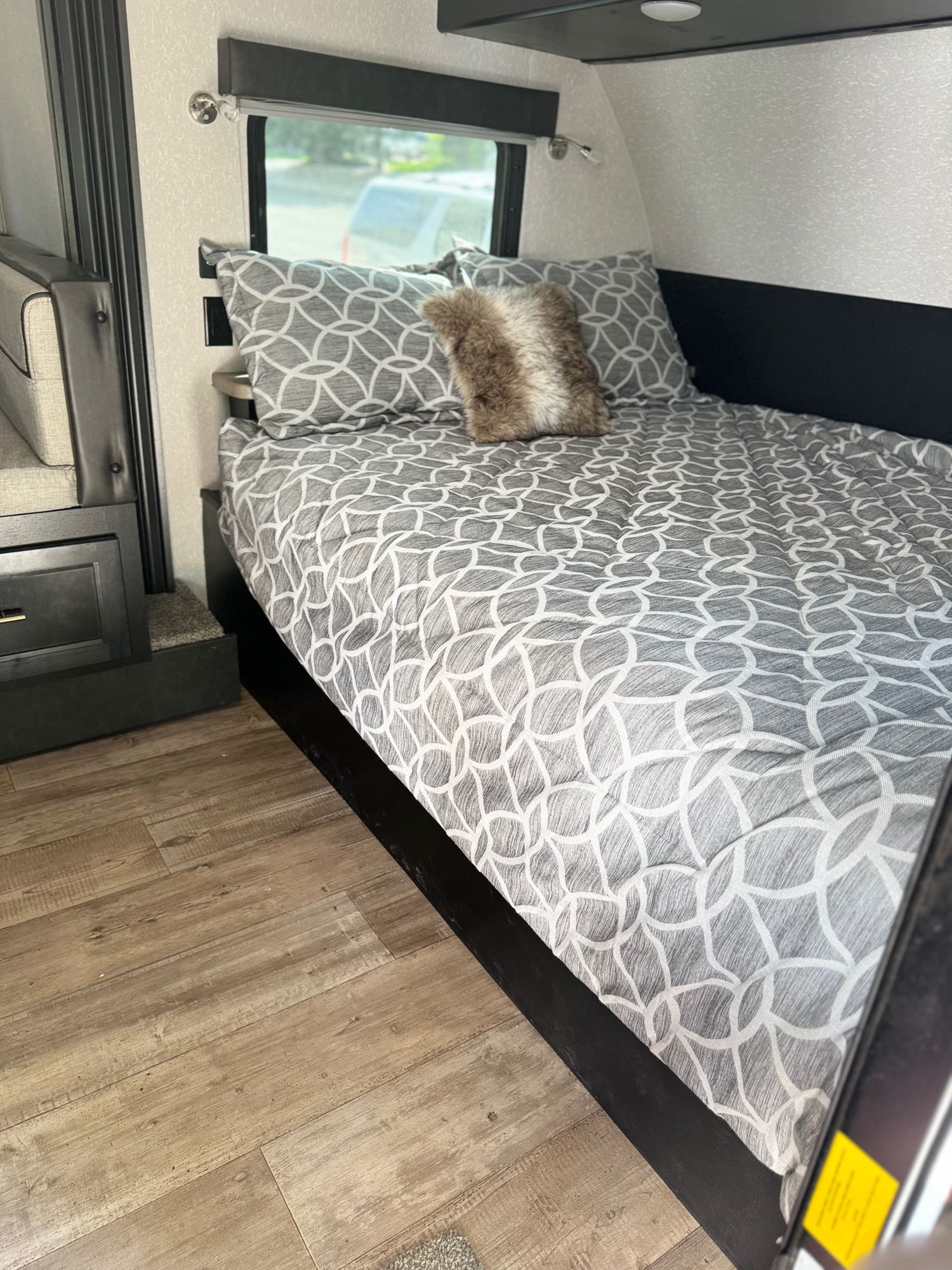 This RV rental interior features a cozy bed with stylish gray bedding and a window for scenic views, ideal for travel comfort.. Forest River Cherokee Wolf Pup Black Label 2022