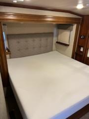 RV rental bedroom with a large bed, white sheets, and a grey tufted headboard, ideal for comfortable travel.. Heartland Bighorn 2017