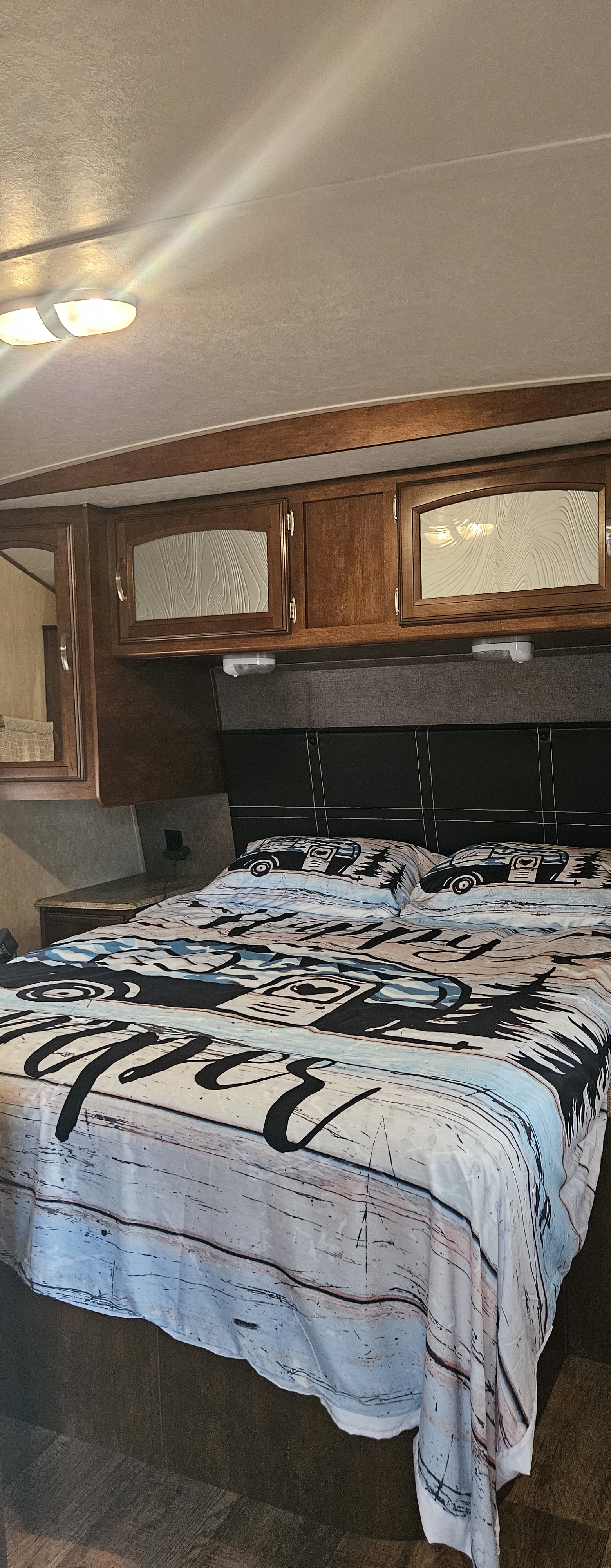 RV rental bedroom features a cozy bed with camping graphics, wooden overhead cabinets, and a headboard.. Forest River Salem Hemisphere Lite 2016