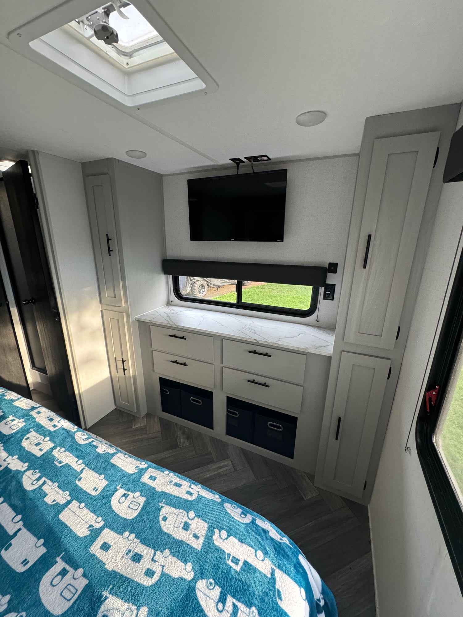 Inside an RV rental bedroom: bed with RV blanket, wall-mounted TV, dresser, and storage. Bright with a skylight.. Forest River Wildwood FSX 2022