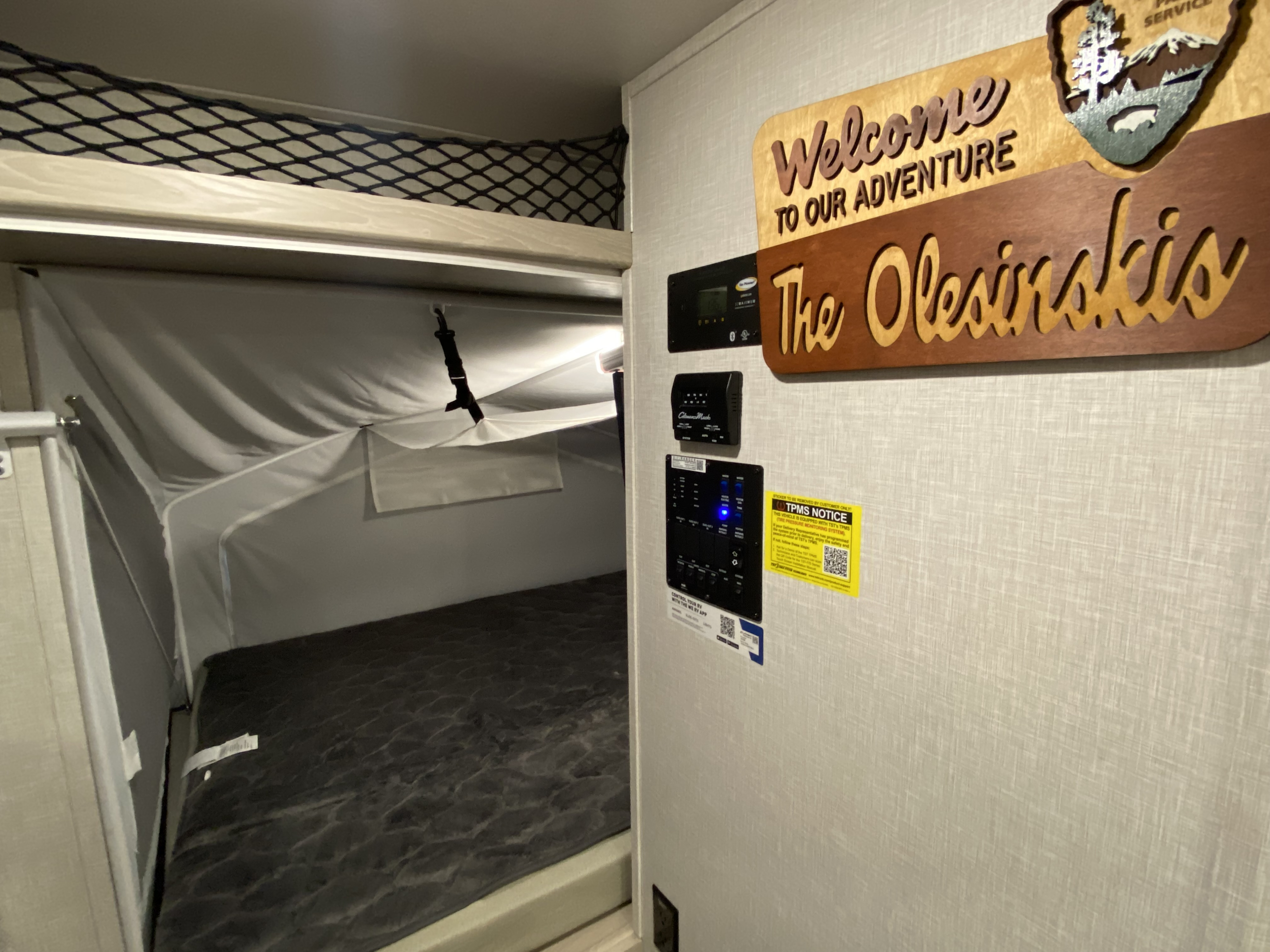 Inside an RV rental: a pop-out bed with safety net, control panel, and a "Welcome to our Adventure" sign.. Forest River Flagstaff Shamrock 2022
