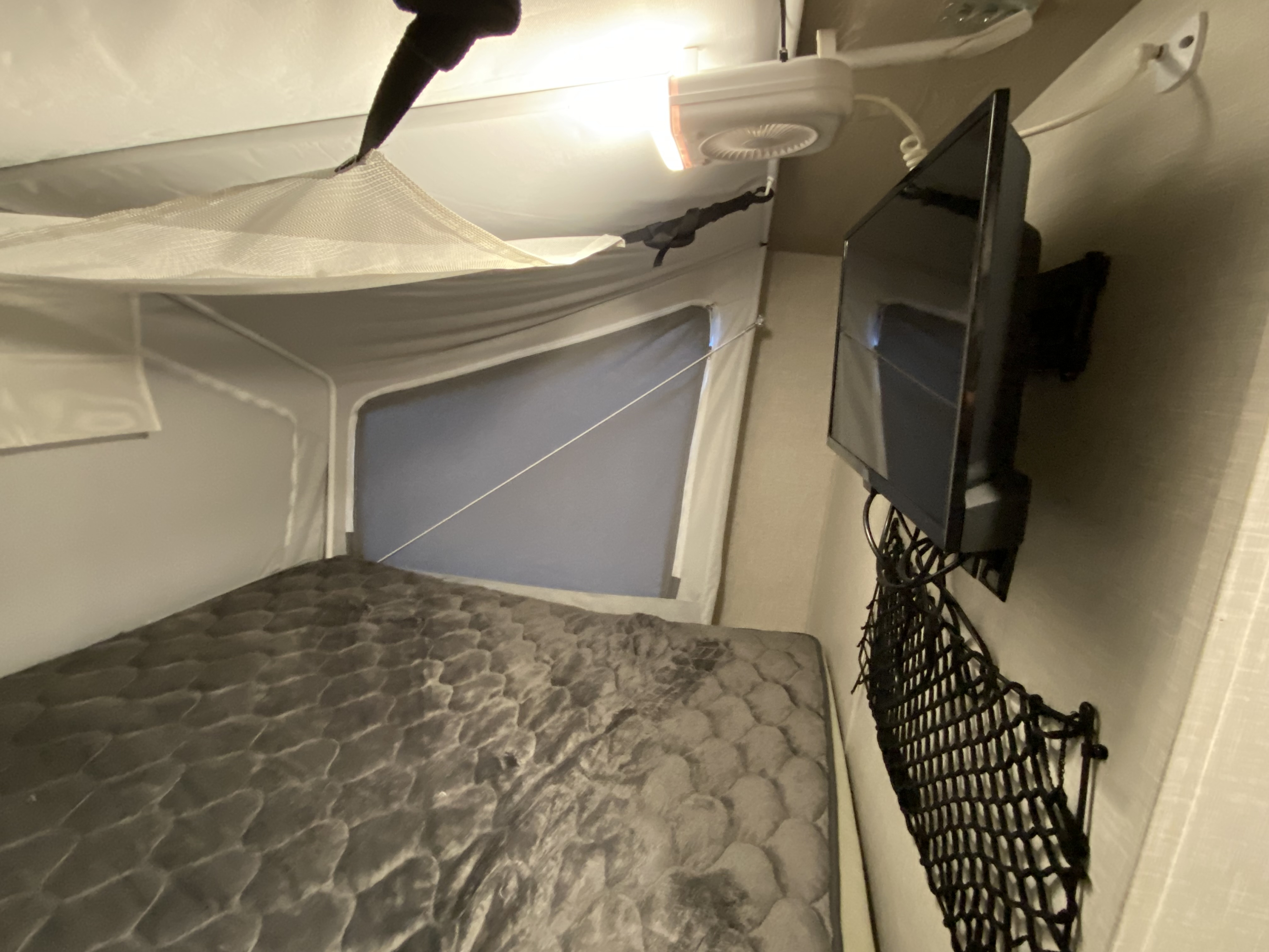 Cozy RV rental interior with a bed, wall-mounted TV, ceiling fan, and mesh storage net. Perfect for a camper's getaway.. Forest River Flagstaff Shamrock 2022