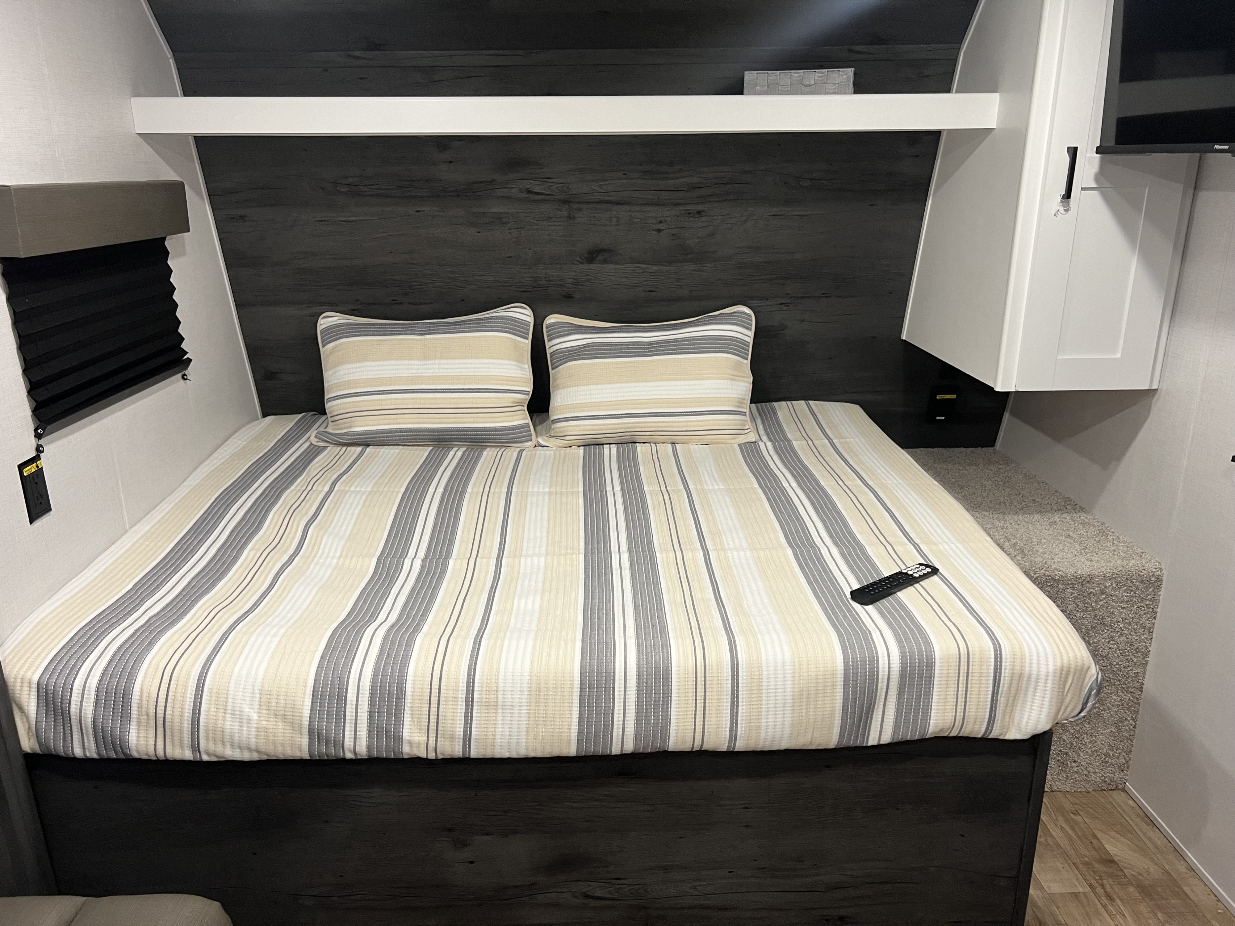 Cozy RV rental bedroom featuring striped bedding, dark wood accents, a window blind, and storage. Ideal for travel.. Keystone RV Hideout 2023