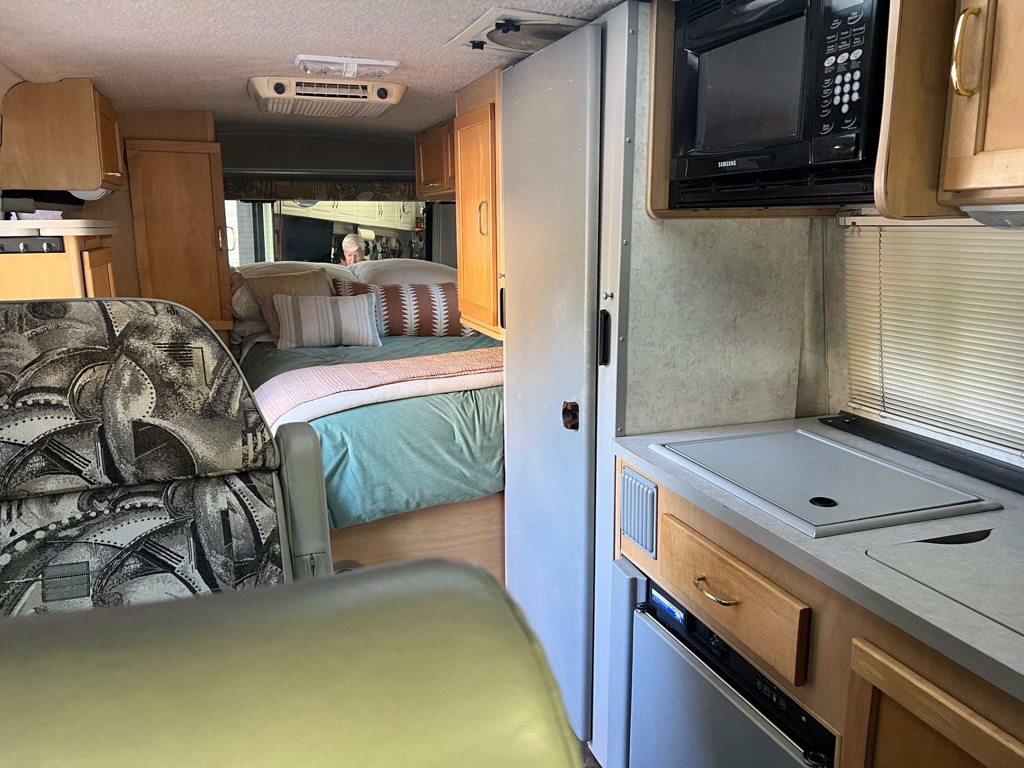 RV rental interior: compact kitchen with microwave/fridge, comfortable bed area, and patterned living space seating.. Winnebago Rialta 2003