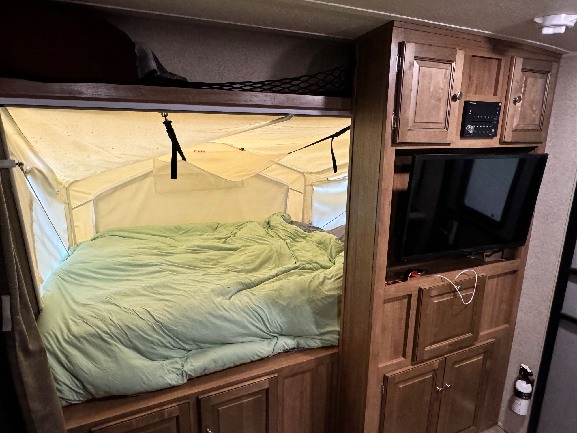 Cozy RV rental bedroom with a pop-out tent bed, wooden cabinetry, TV, and storage. Perfect for camping trips.. Forest River Rockwood Roo 2018