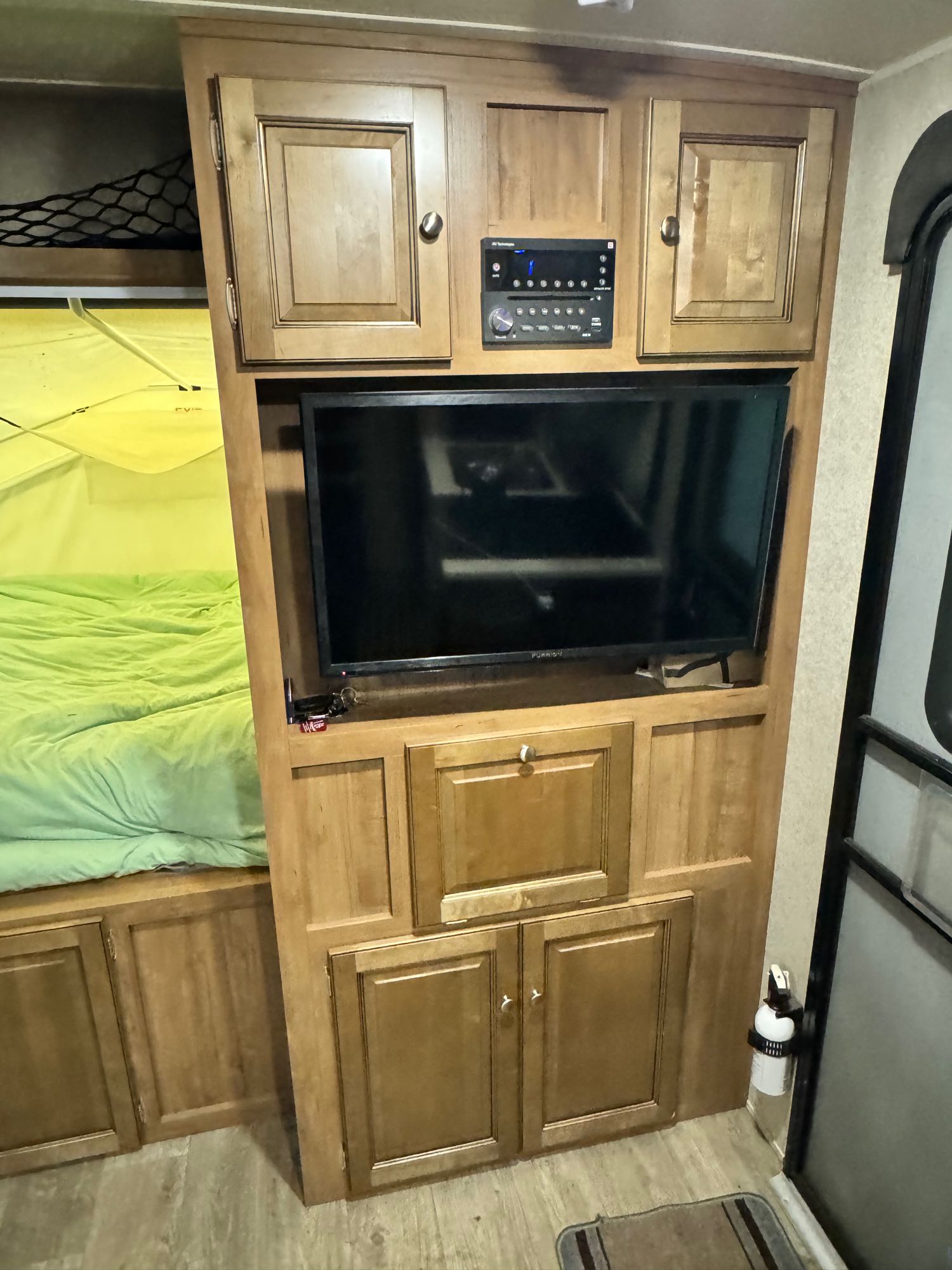 Inside an RV rental: a bunk bed with green bedding, TV, stereo, wood cabinets, and a fire extinguisher mounted by the door.. Forest River Rockwood Roo 2018