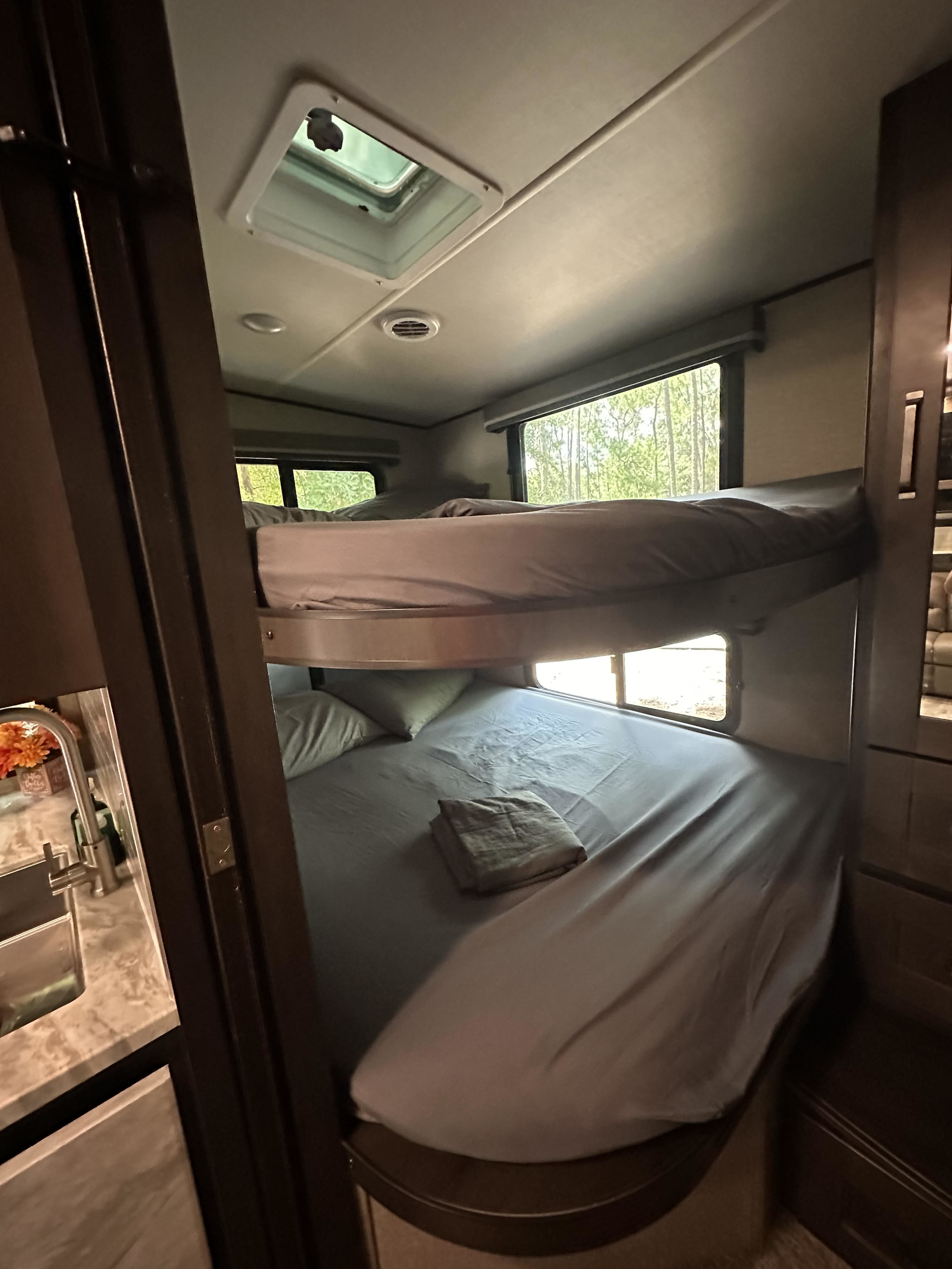 Cozy RV rental interior with bunk beds, offering a serene nature view through windows. Ideal for family adventures.. Grand Design Reflection 2021