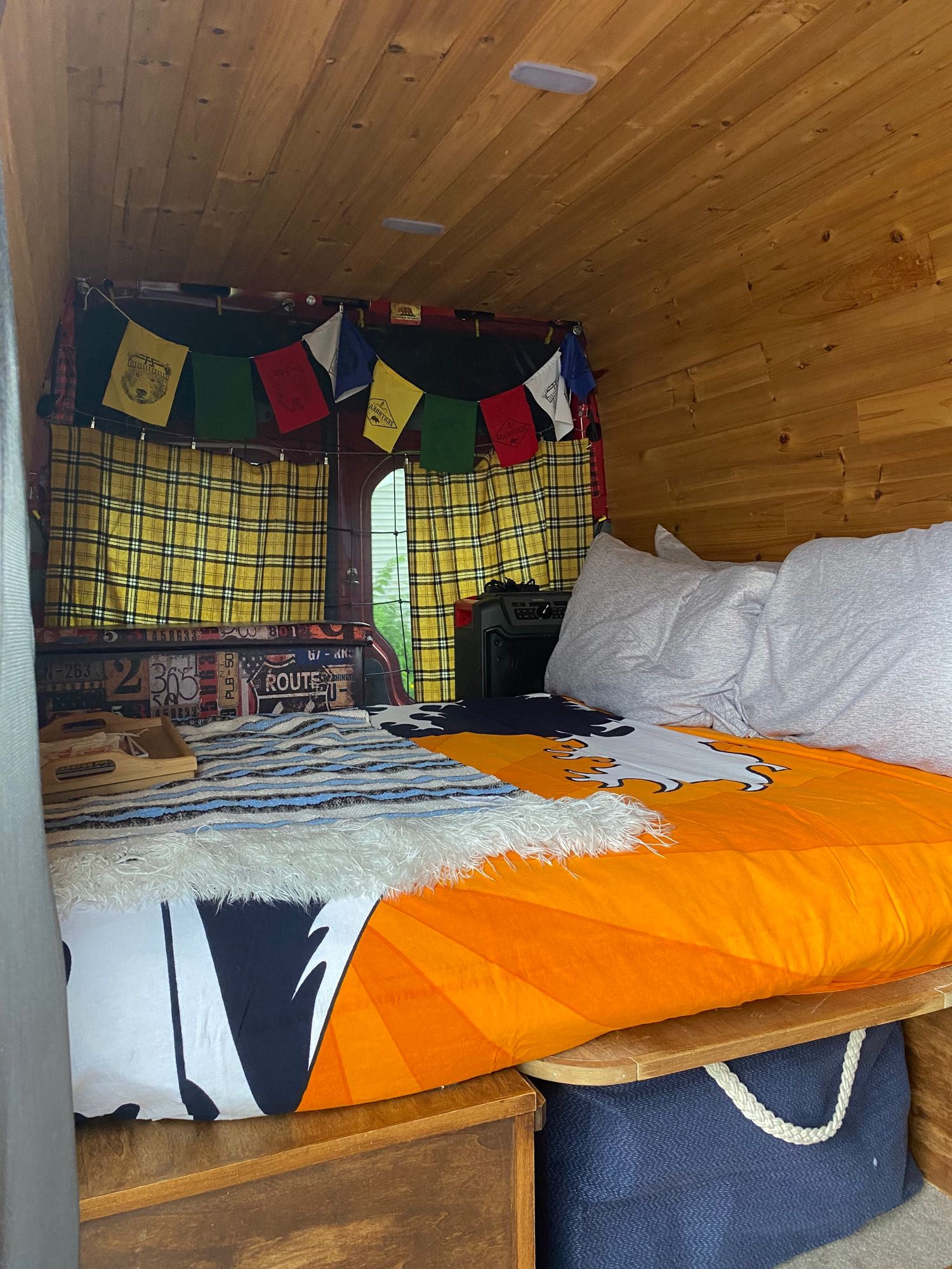 Cozy RV rental bedroom with wood paneling, an orange-patterned bed, plaid curtains, and a unique license plate headboard.. Mercedes Sprinter 2015