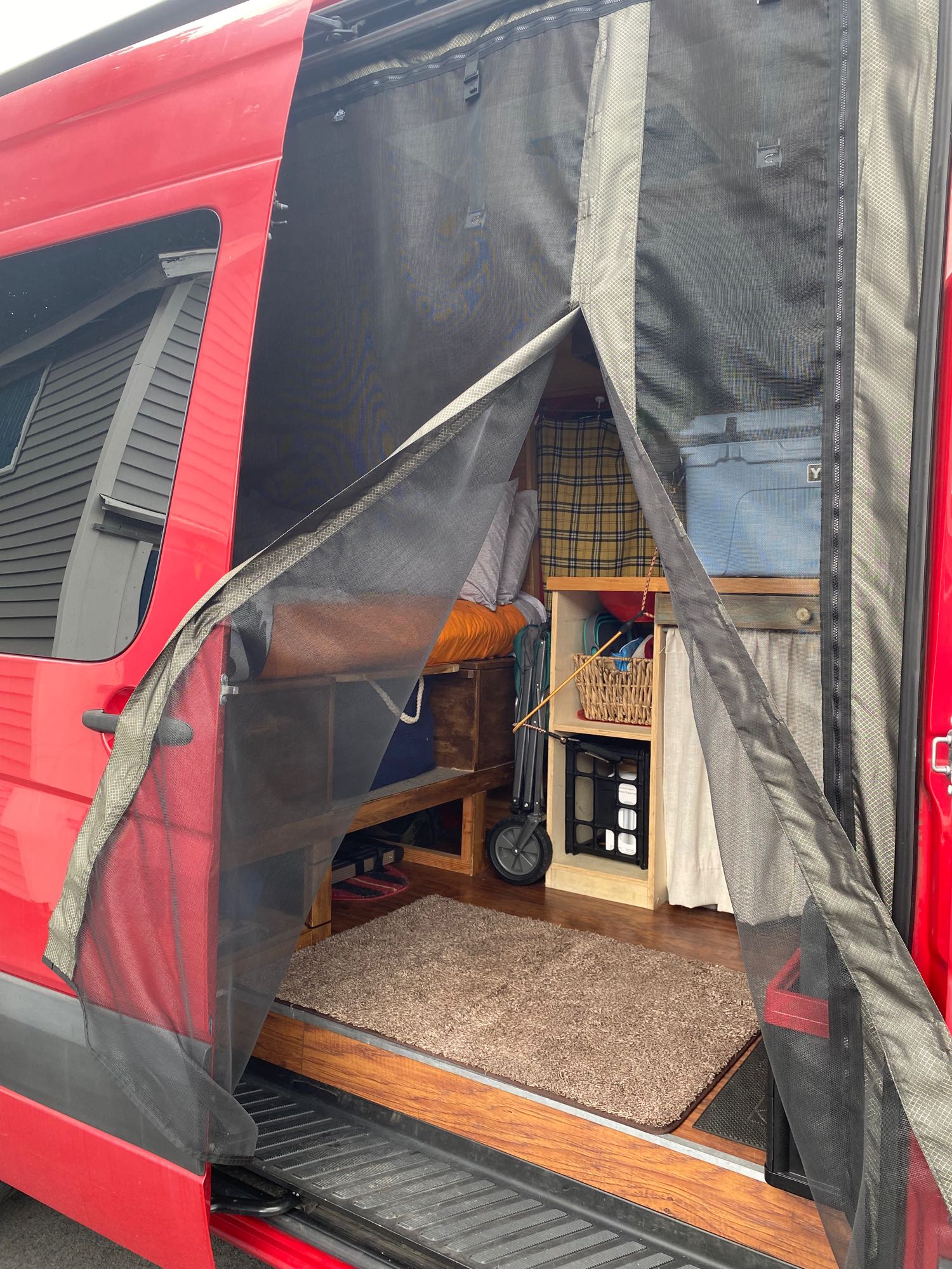 Inside an rv rental camper van: mesh screen door open to reveal organized storage, wood floor, and cozy interior details.. Mercedes Sprinter 2015