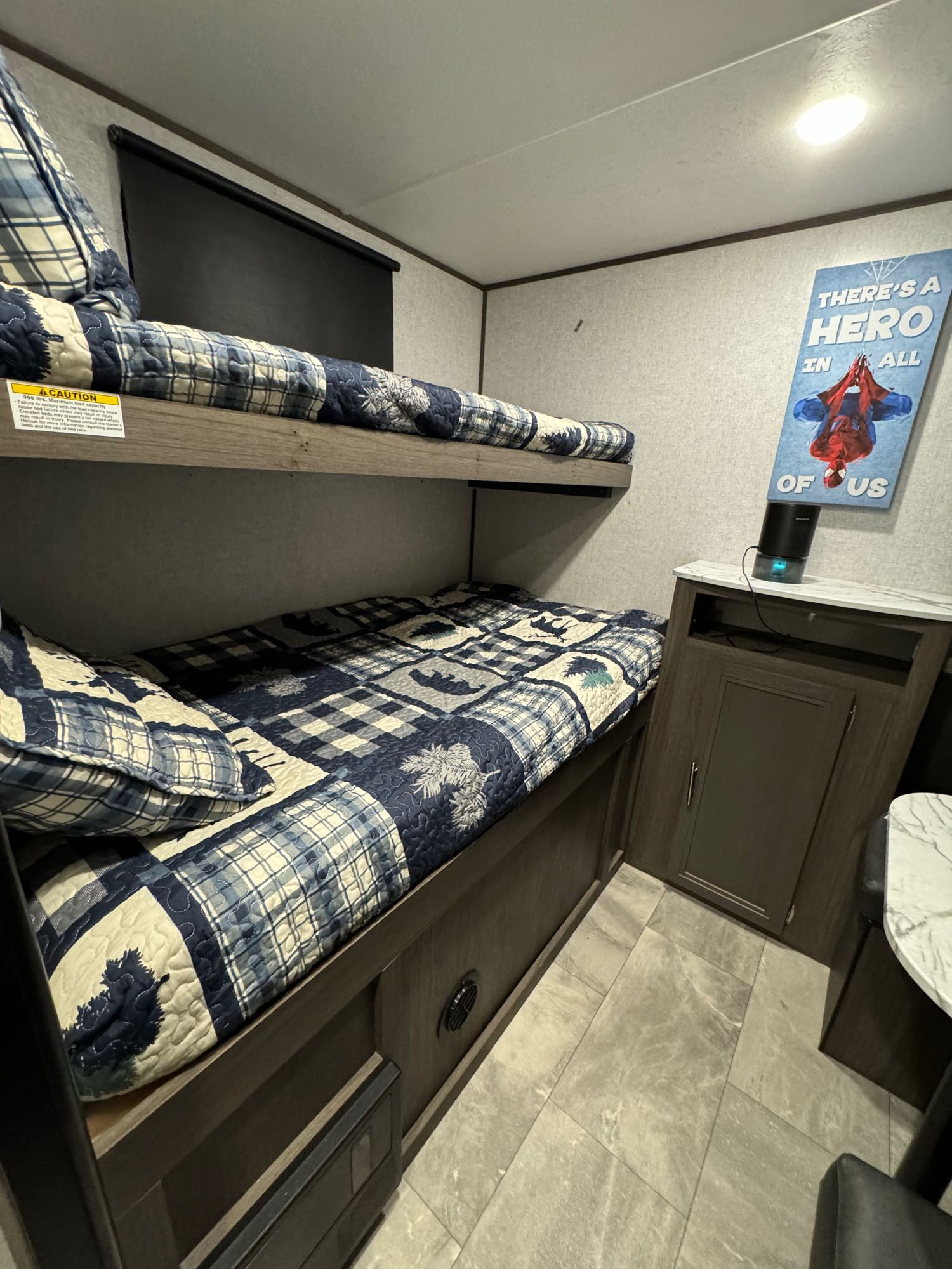 RV rental bunk beds featuring a fun Spider-Man poster and a cozy blue quilt, perfect for family adventures.. Dutchmen Kodiak Ultra Lite 2021