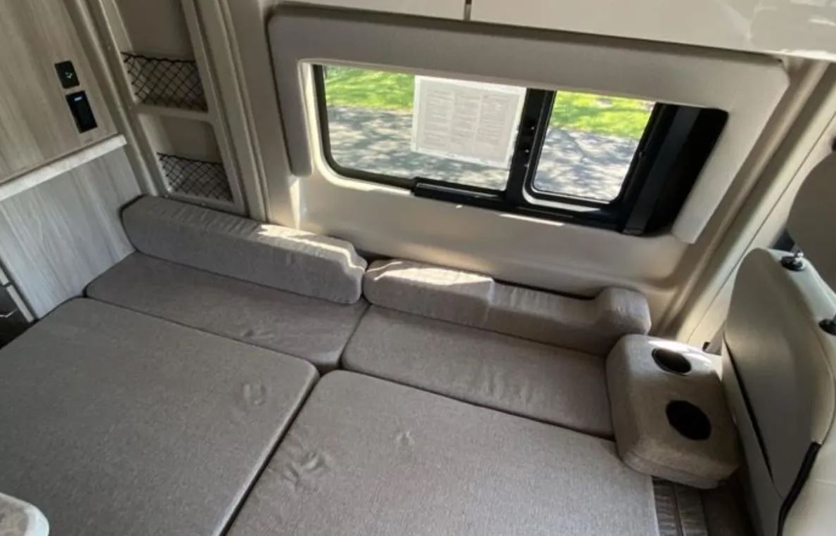 Spacious RV rental interior with convertible seating laid out as a comfortable bed. Features include a large window, storage nets, and cup holders.. Thor Scope 2023