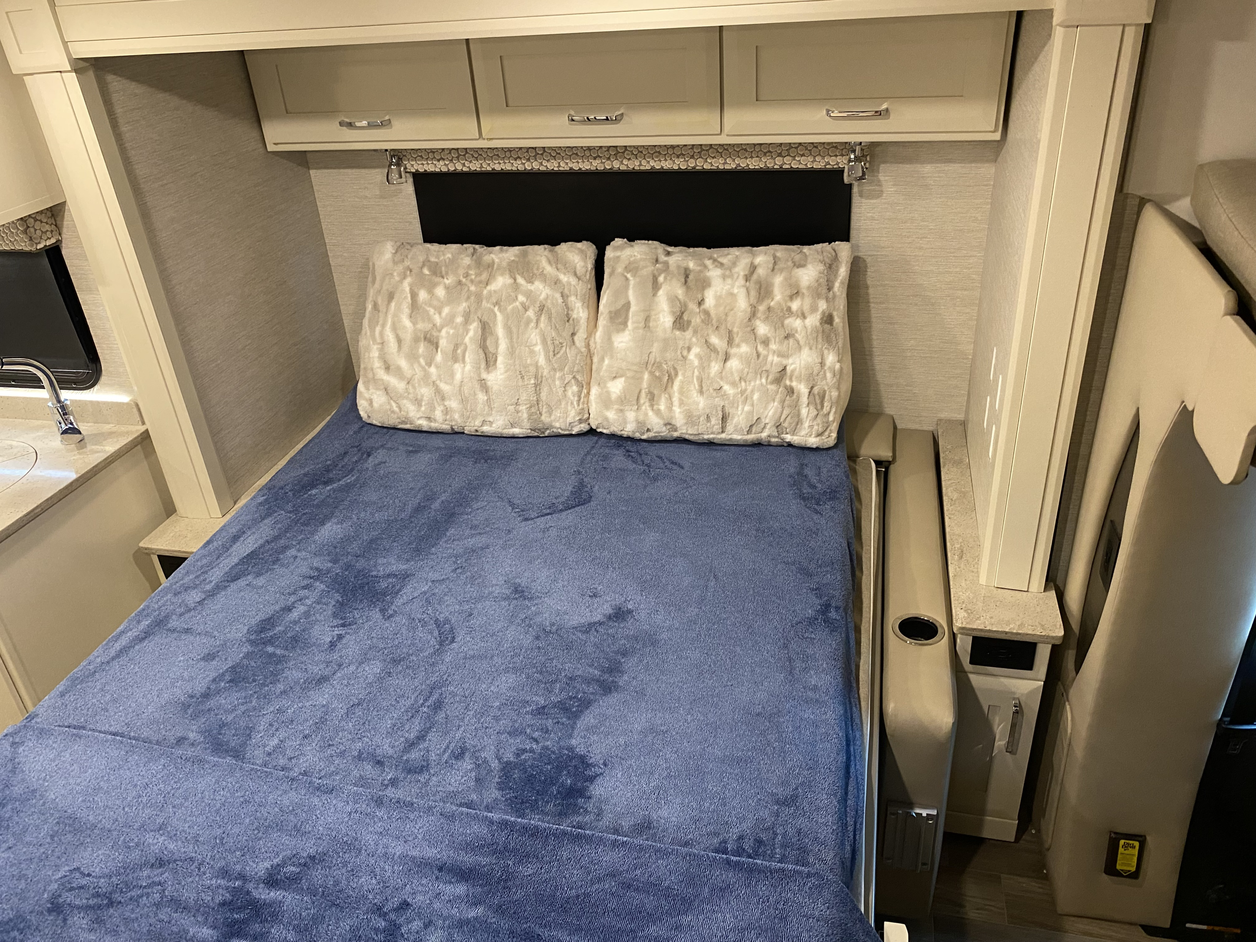 Inside an RV rental: Plush blue blanket on the bed, overhead storage, and kitchen sink visible.. Tiffin wayfarer 2022
